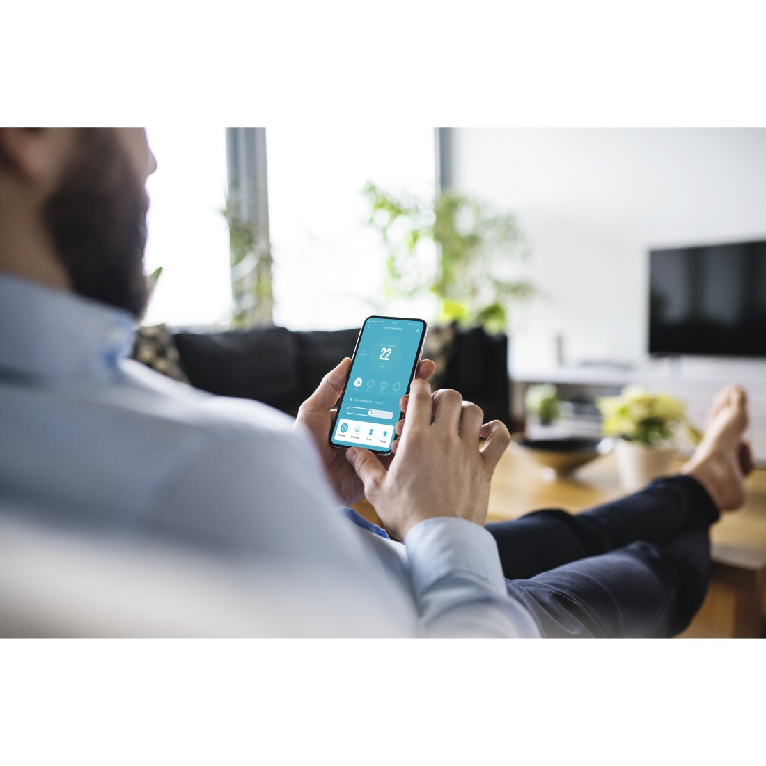 Ein Mann benutzt ein Smartphone, um ein Smart-Home-System zu steuern, das Telefon zeigt Temperatur.