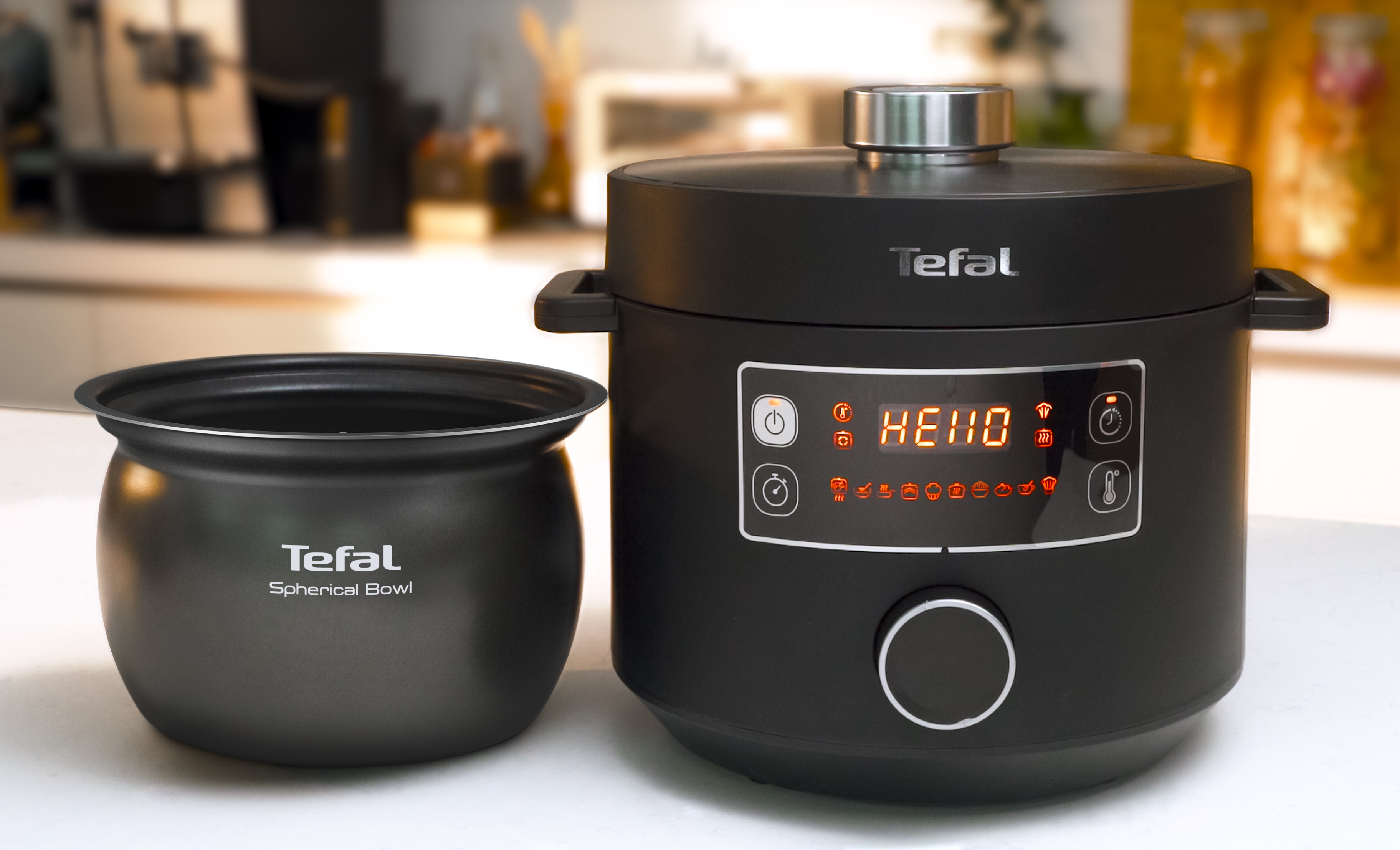 Ein schwarzer Tefal Multikocher und eine schwarze kugelförmige Schüssel. Der Kocher zeigt 'HELLO' an.