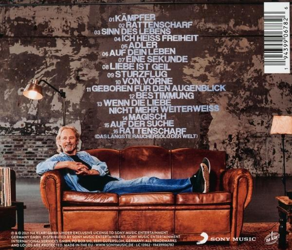 Mann im Jeanshemd auf braunem Ledersofa, vor strukturierter Wand mit Text und Lampe.