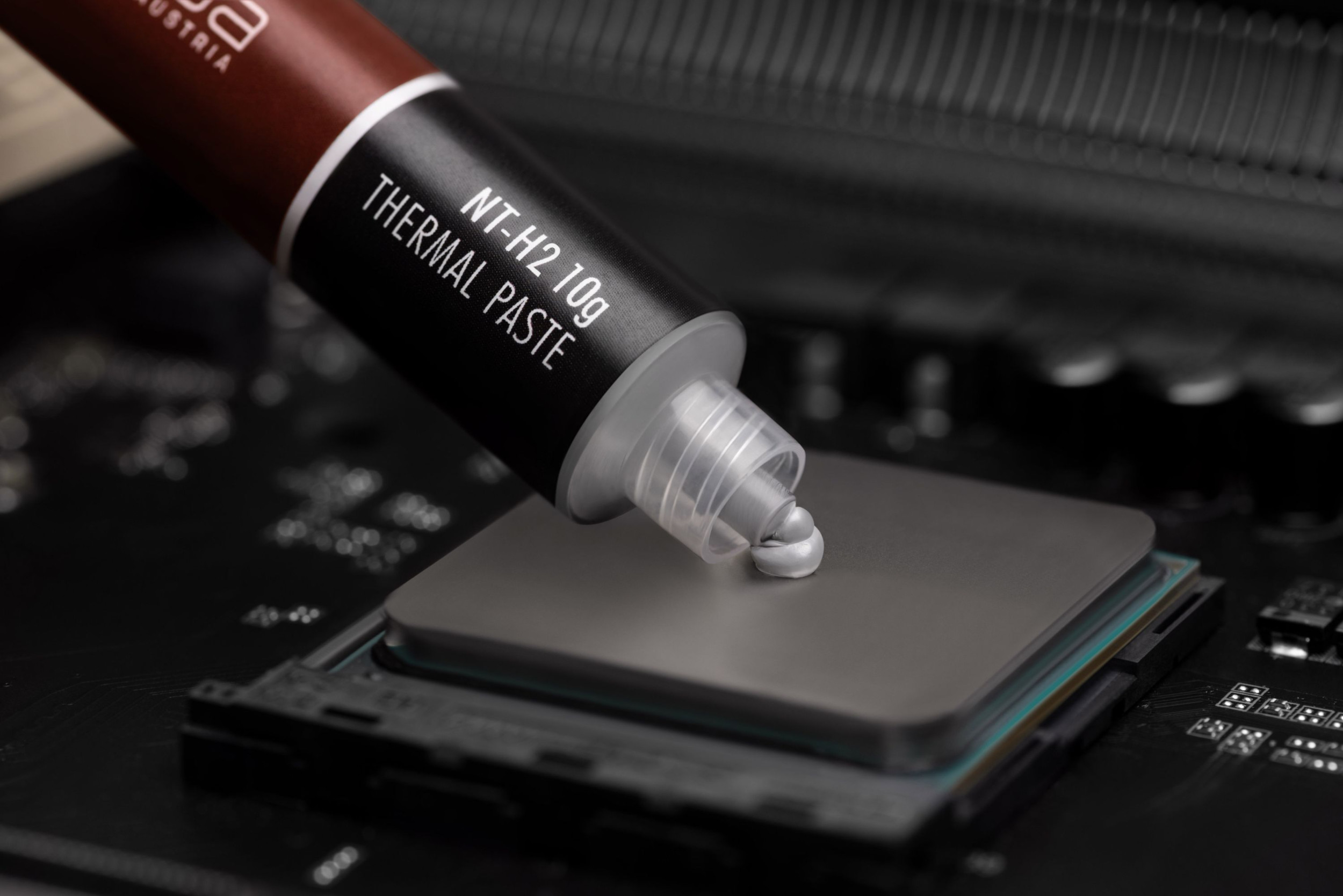 Wärmeleitpaste wird auf eine CPU auf einem Motherboard aufgetragen, wobei die Tube und die Verpackung sichtbar sind.