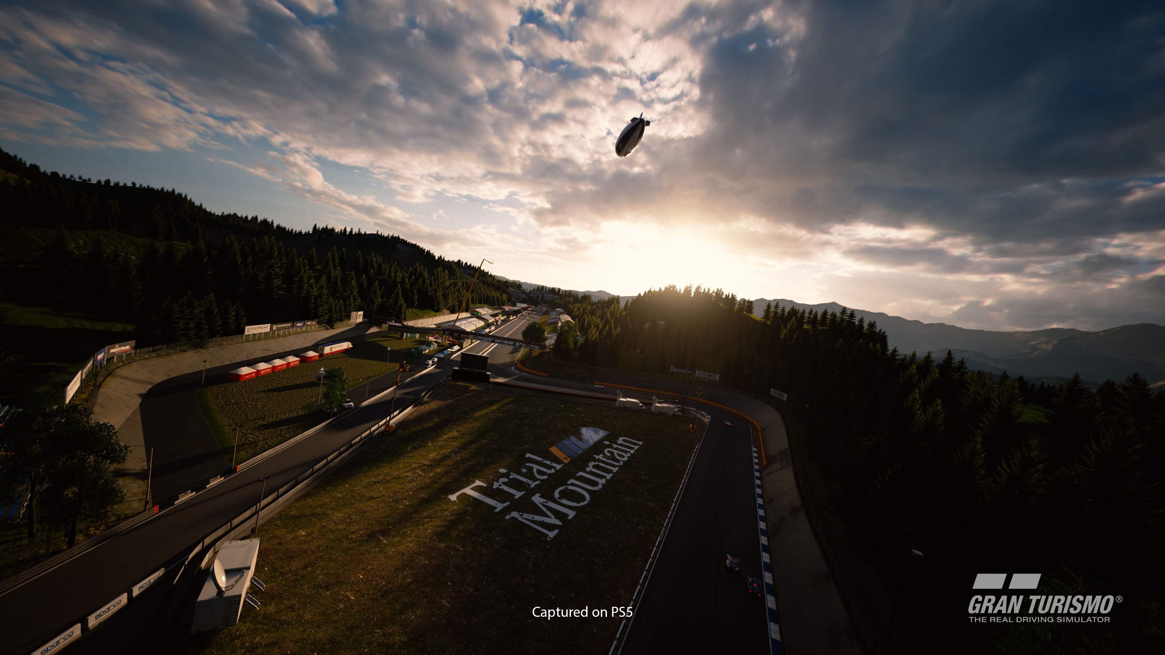 Vue aérienne d'un circuit de course en milieu montagneux avec un dirigeable et un coucher de soleil.