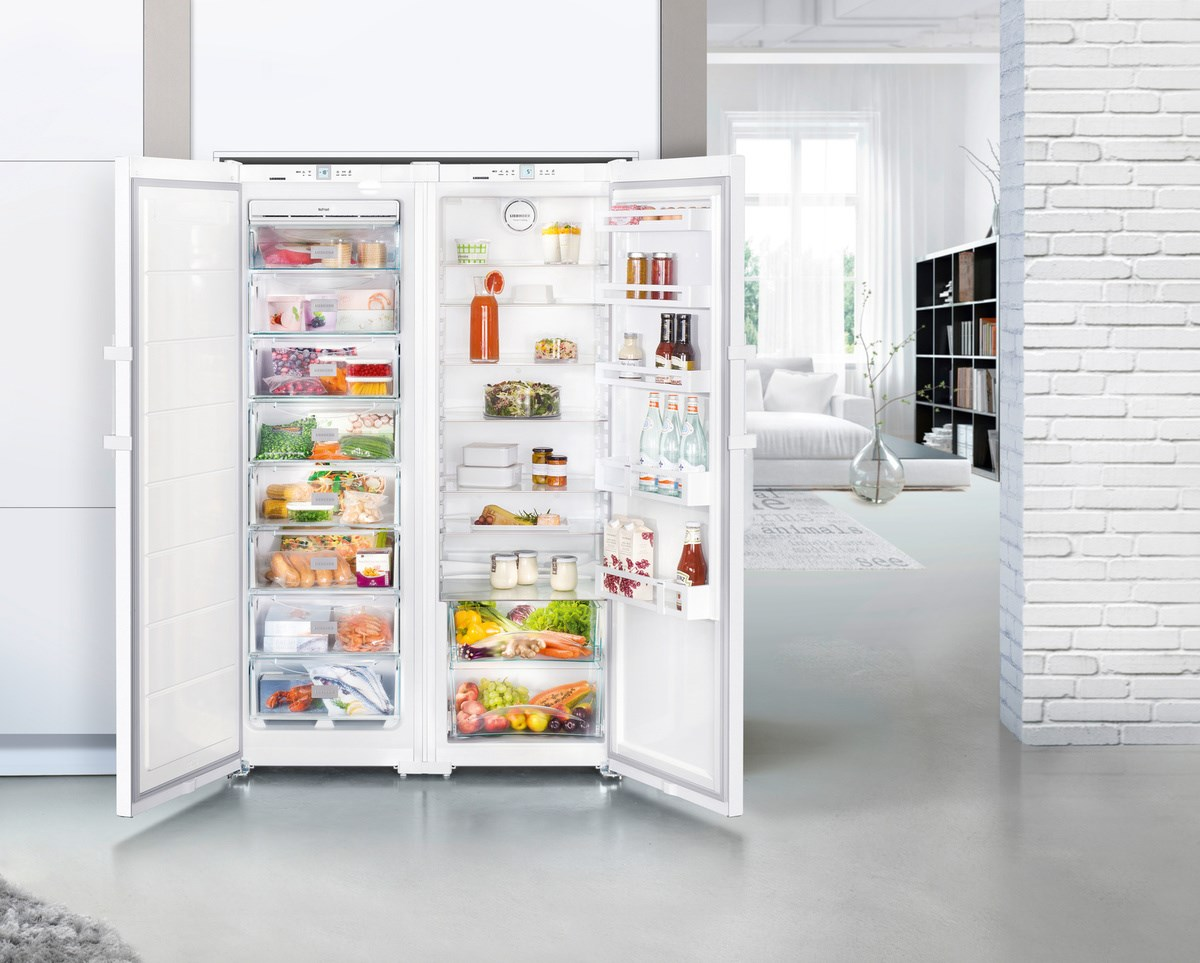 Refrigerador blanco abierto que muestra alimentos envasados. Incluye verduras, frutas, bebidas y congelados.