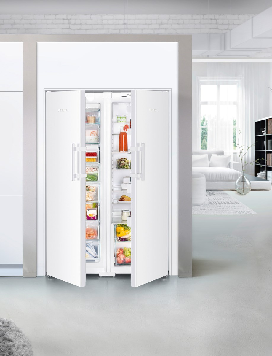 Refrigerador blanco con puertas abiertas que revelan alimentos en recipientes transparentes, habitación en el fondo.
