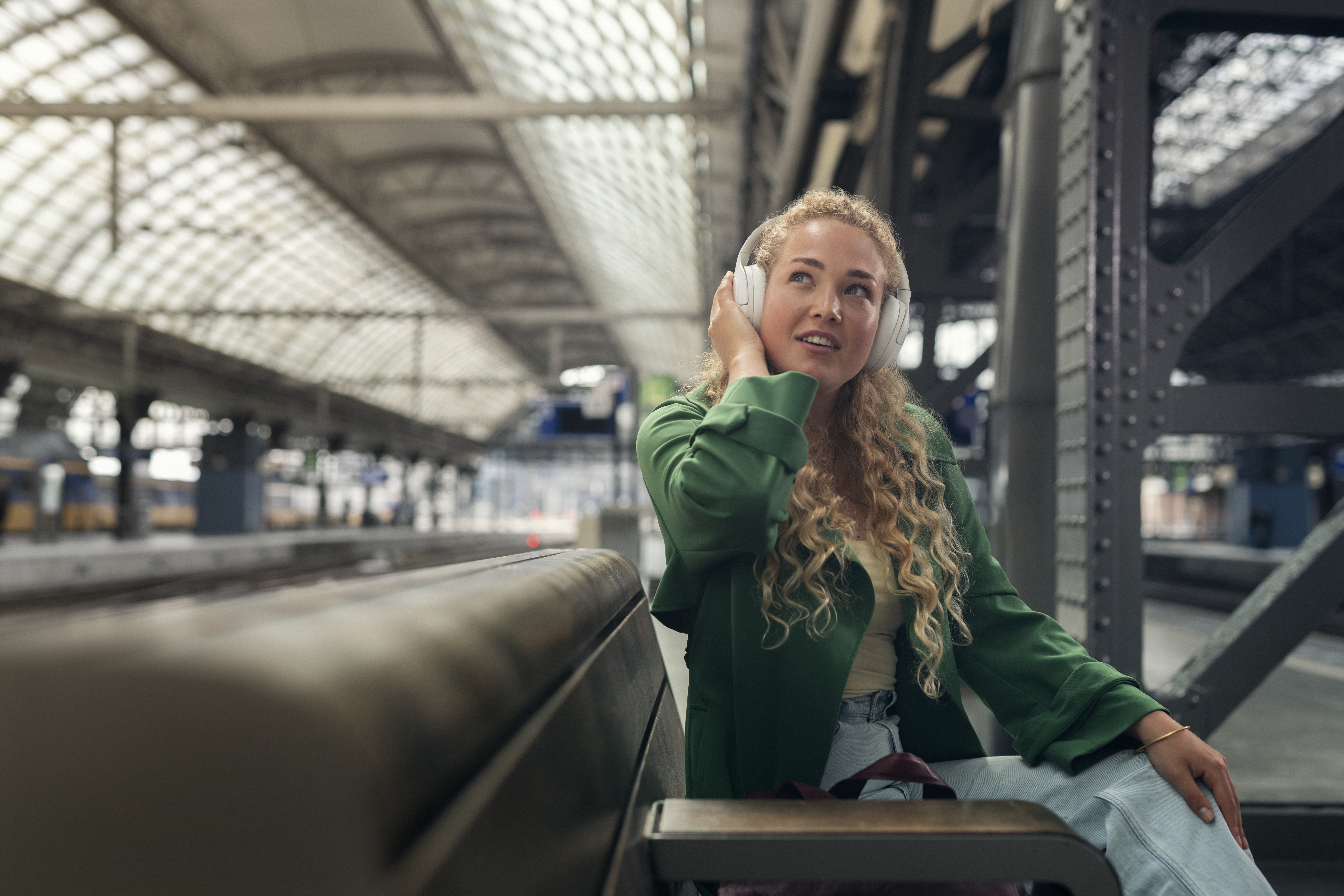 Eine Frau mit Kopfhörern hört Musik an einem Bahnhof.