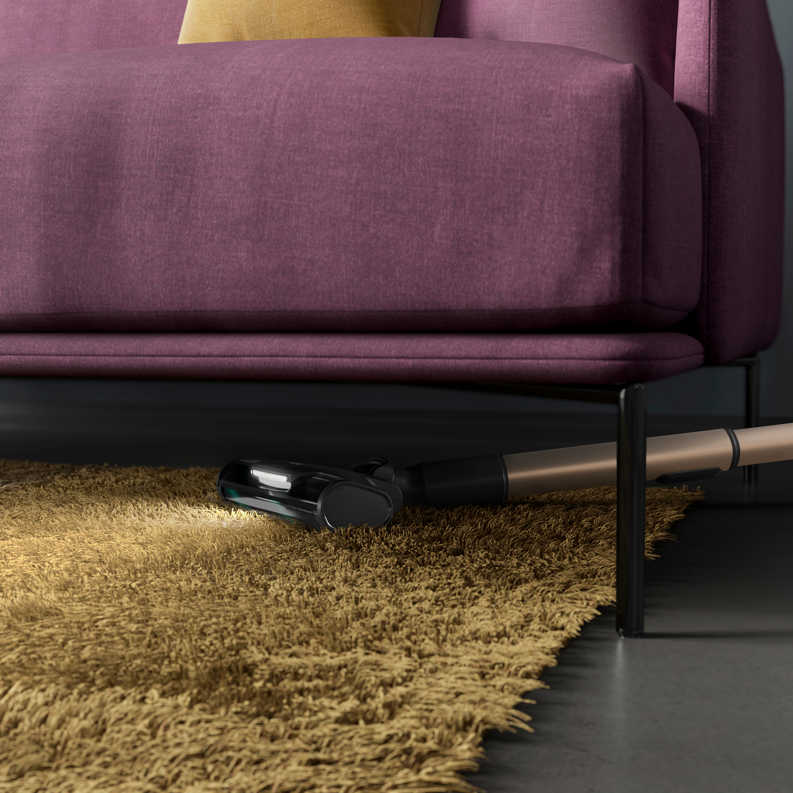 Staubsaugerkopf, der einen Teppich unter einem lila Sofa reinigt. Tan-Teppich und dunkler Boden im Vordergrund.