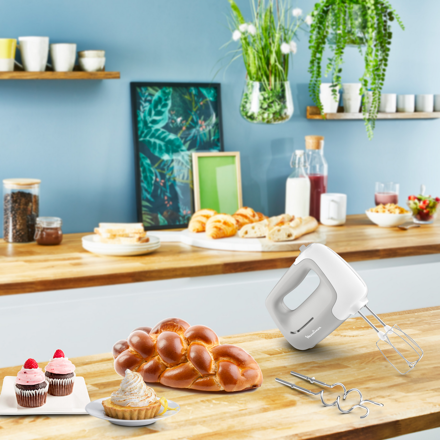 Escena de cocina con productos horneados, una batidora y plantas en estantes.