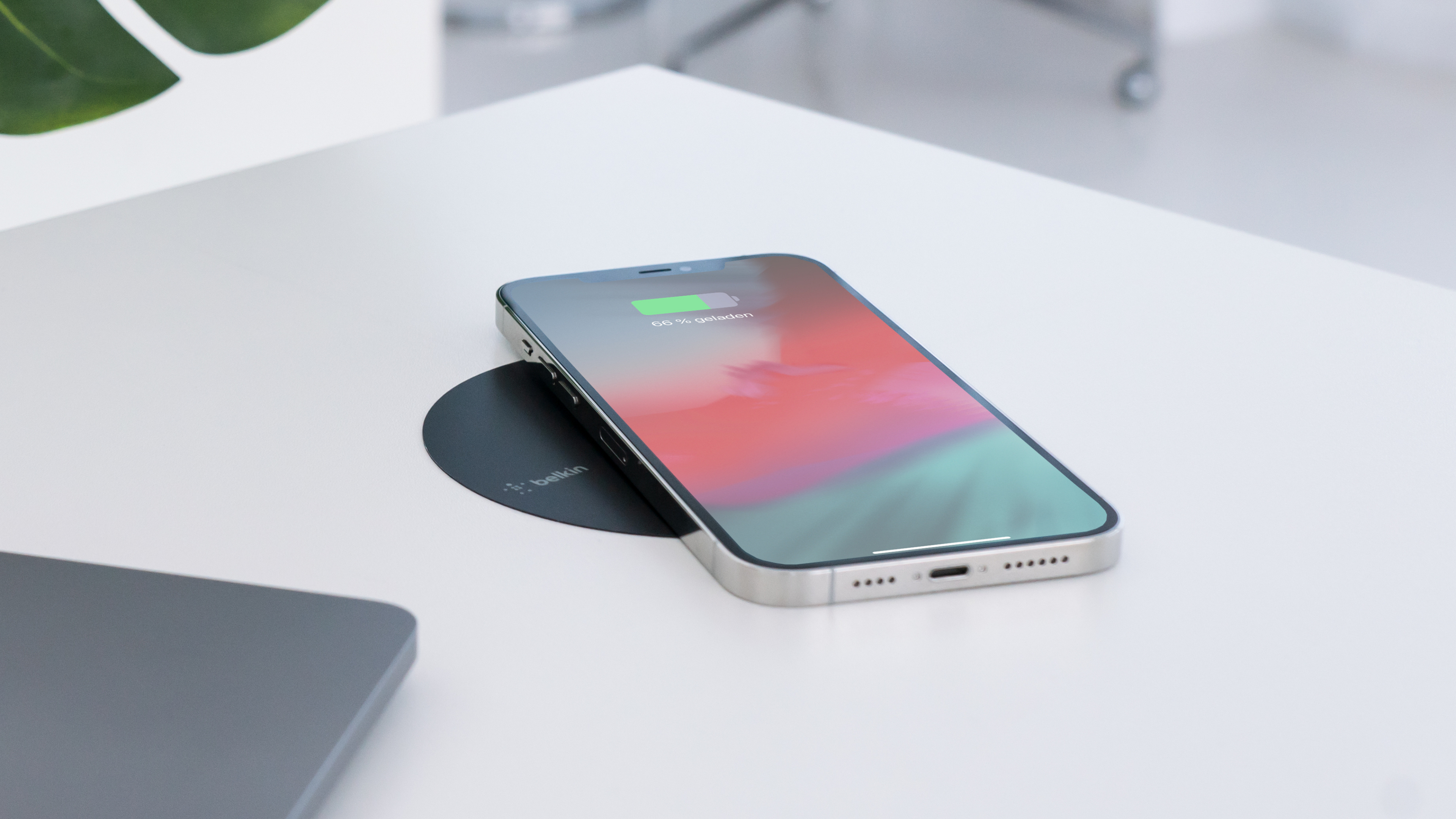 Telefon auf weißem Schreibtisch, der kabellos geladen wird. Der Schreibtisch hat ein eingebautes Ladegerät.