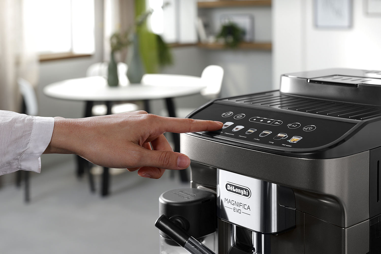 Een hand drukt op een knop van een zwart-grijze koffiemachine.