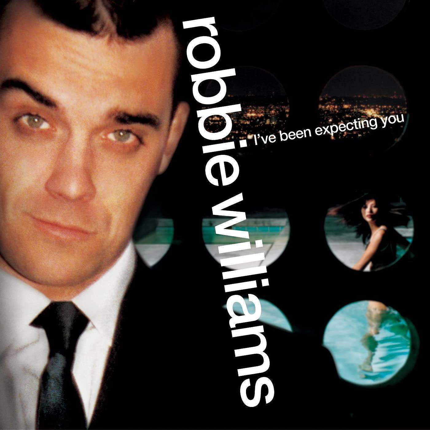 Robbie Williams öltönyben, városra néző körökkel, nővel és medencével.