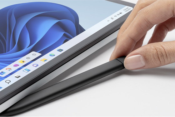 Hand, die einen Stift in der Nähe eines Laptops hält. Der Stift ist schwarz und der Laptop befindet sich auf weißem Grund.