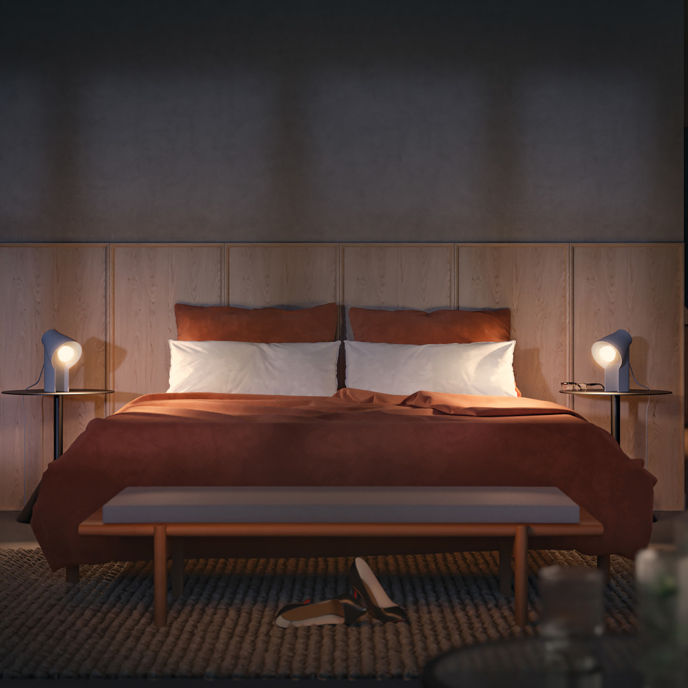 Une scène de chambre. Un lit avec une couverture orange brûlé, deux lampes sur les tables de chevet, un banc et un tapis.