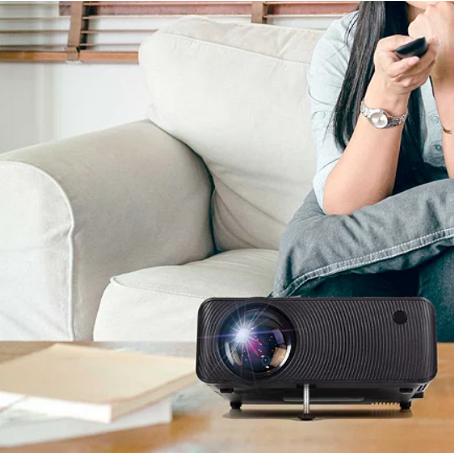 Un proyector negro está sobre una mesa frente a un sofá, con libros al lado.