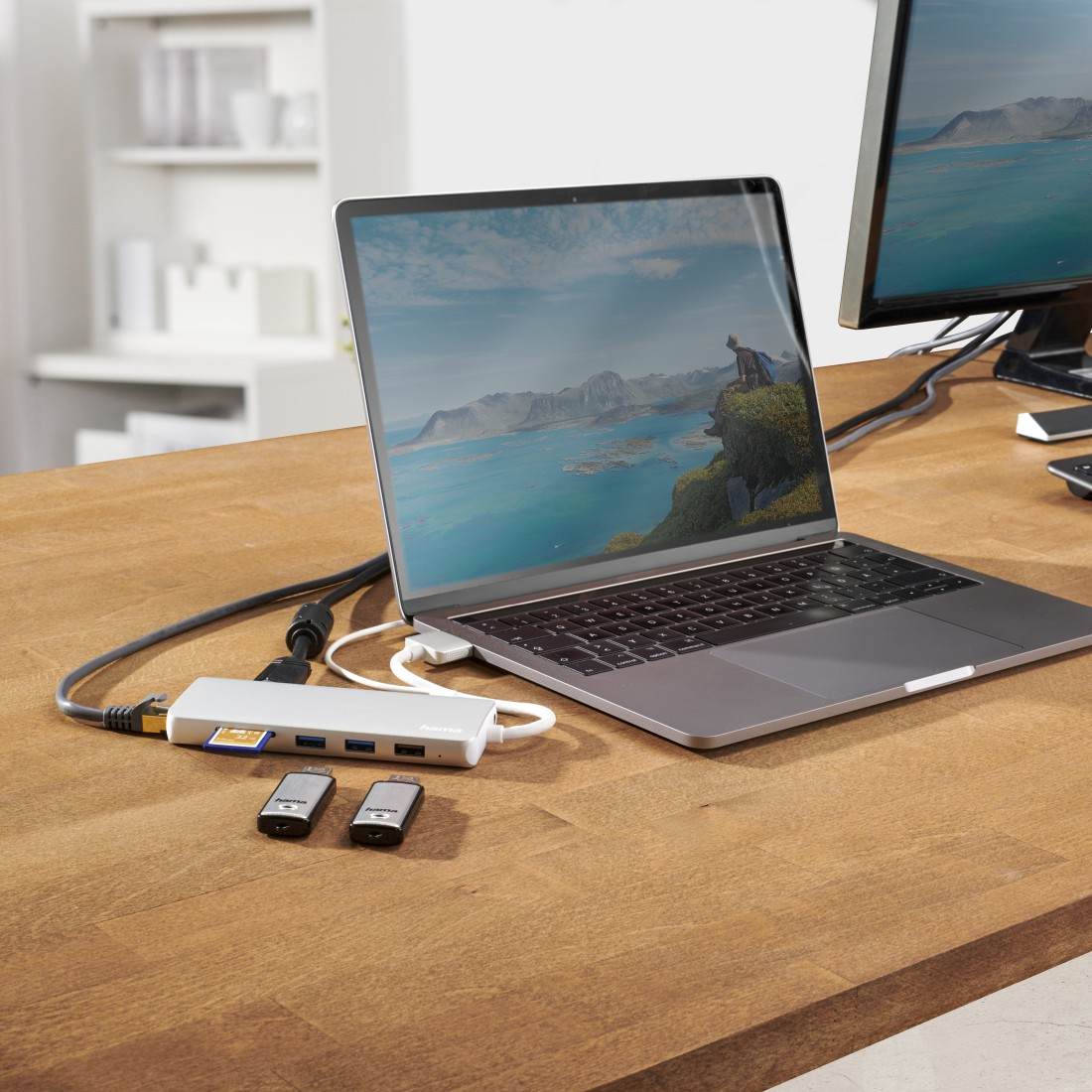 Laptop und Hub mit Monitor verbunden. Zwei externe Laufwerke sind sichtbar, auf dem Schreibtisch.