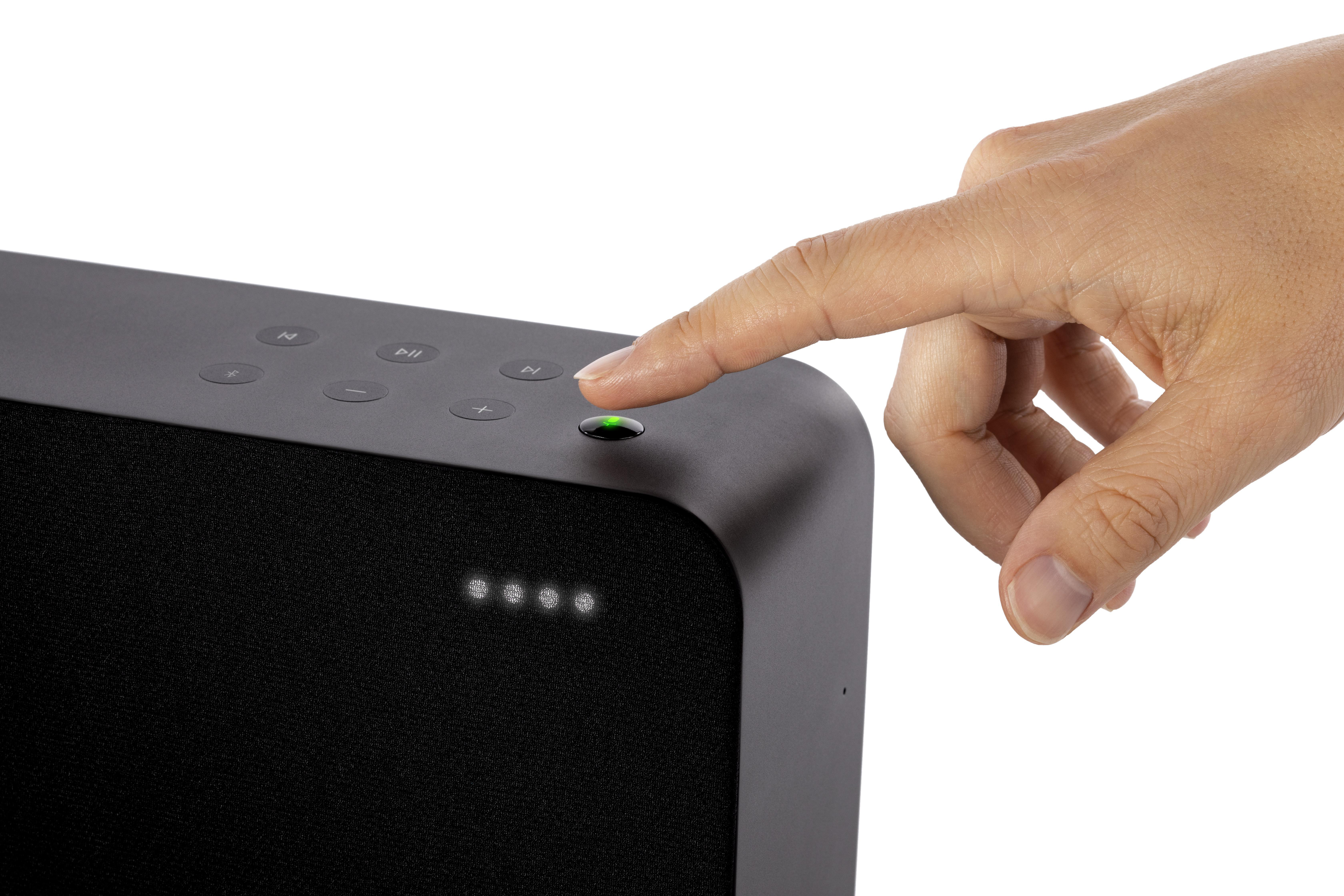 Hand drückt Knopf auf dunkelgrauem Lautsprecher.