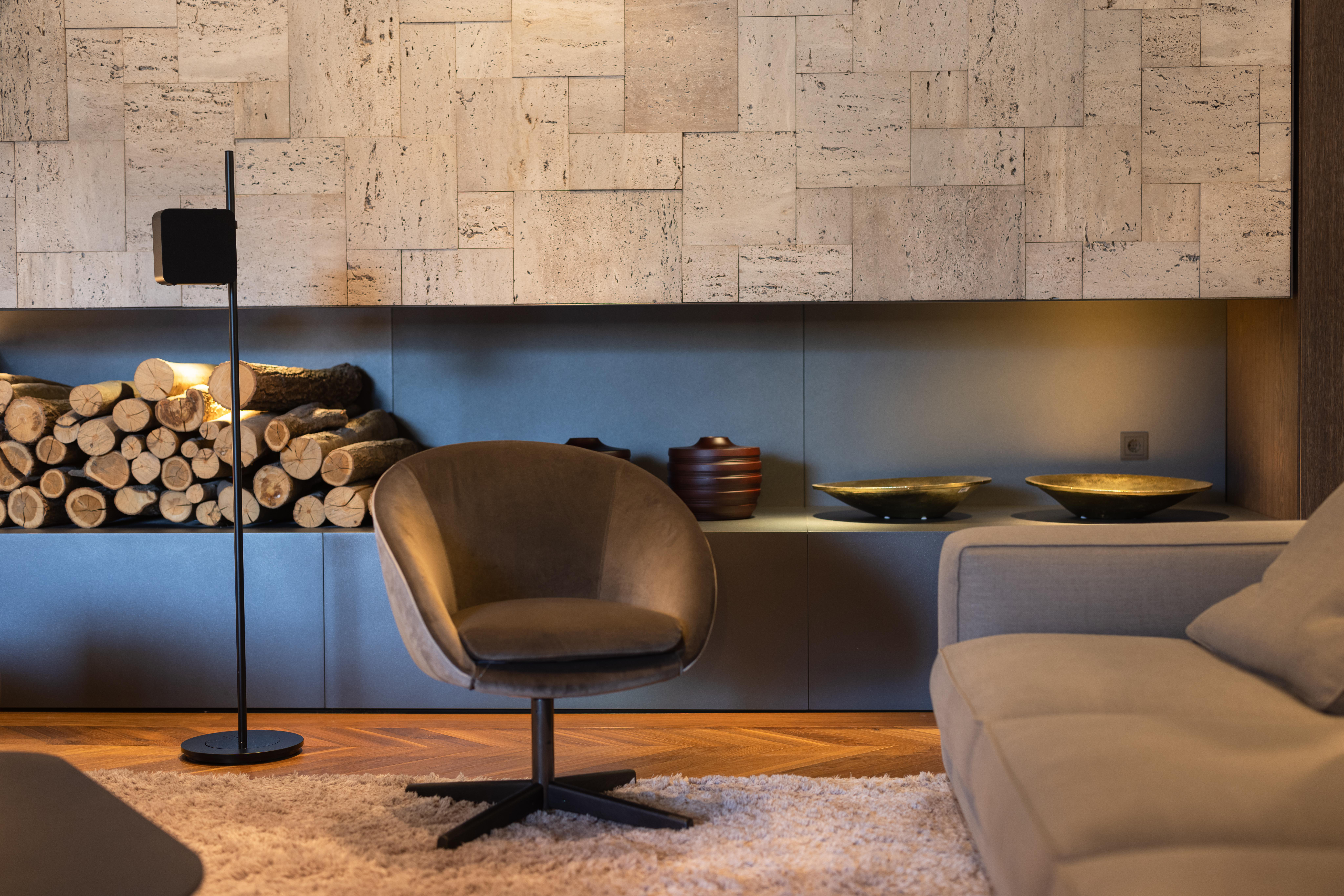 Wohnzimmer mit Sessel, Sofa, Kamin, Brennholz und Dekorationsartikeln.