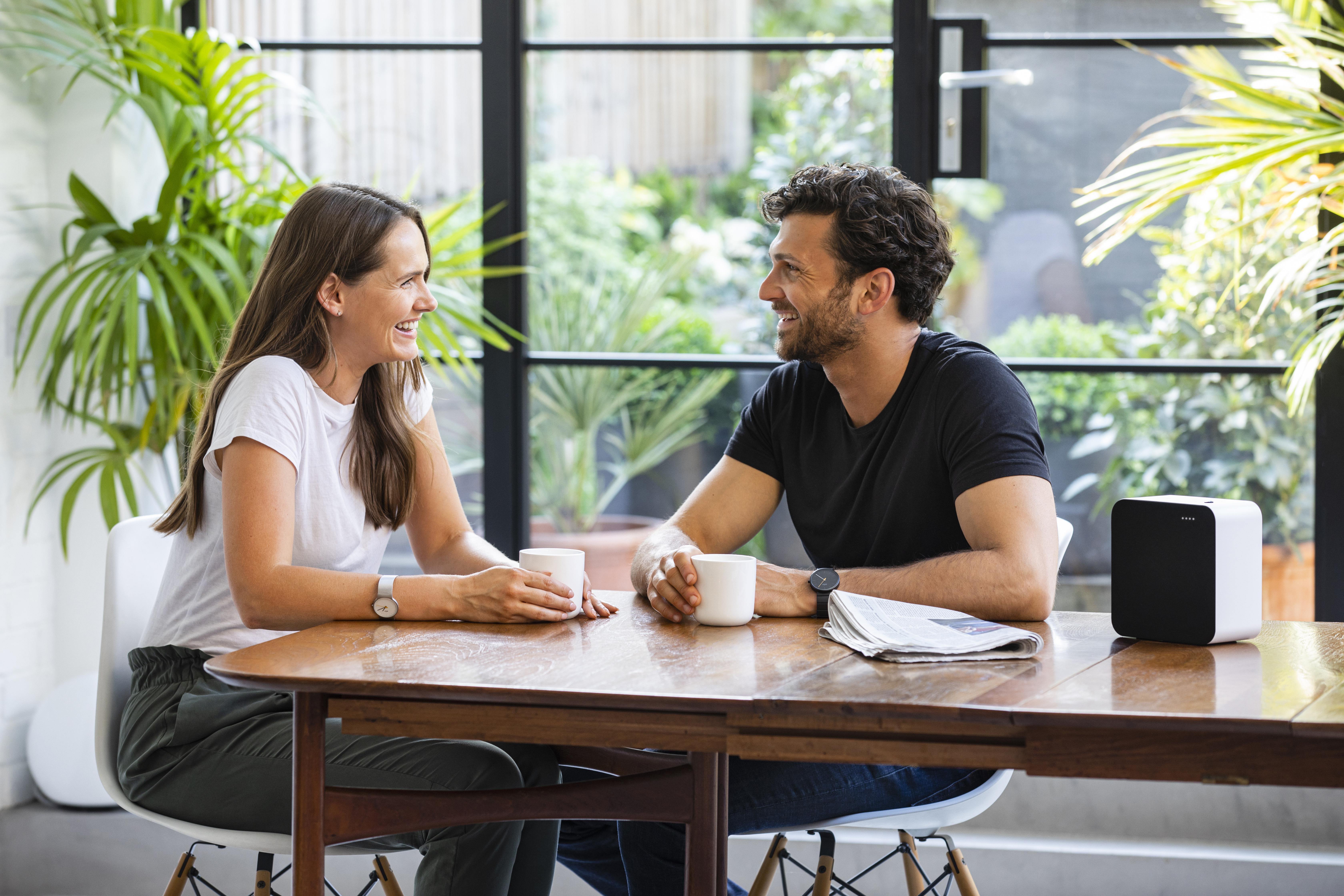 Ein Paar sitzt an einem Tisch, lächelt und unterhält sich. Auf dem Tisch steht ein Lautsprecher.