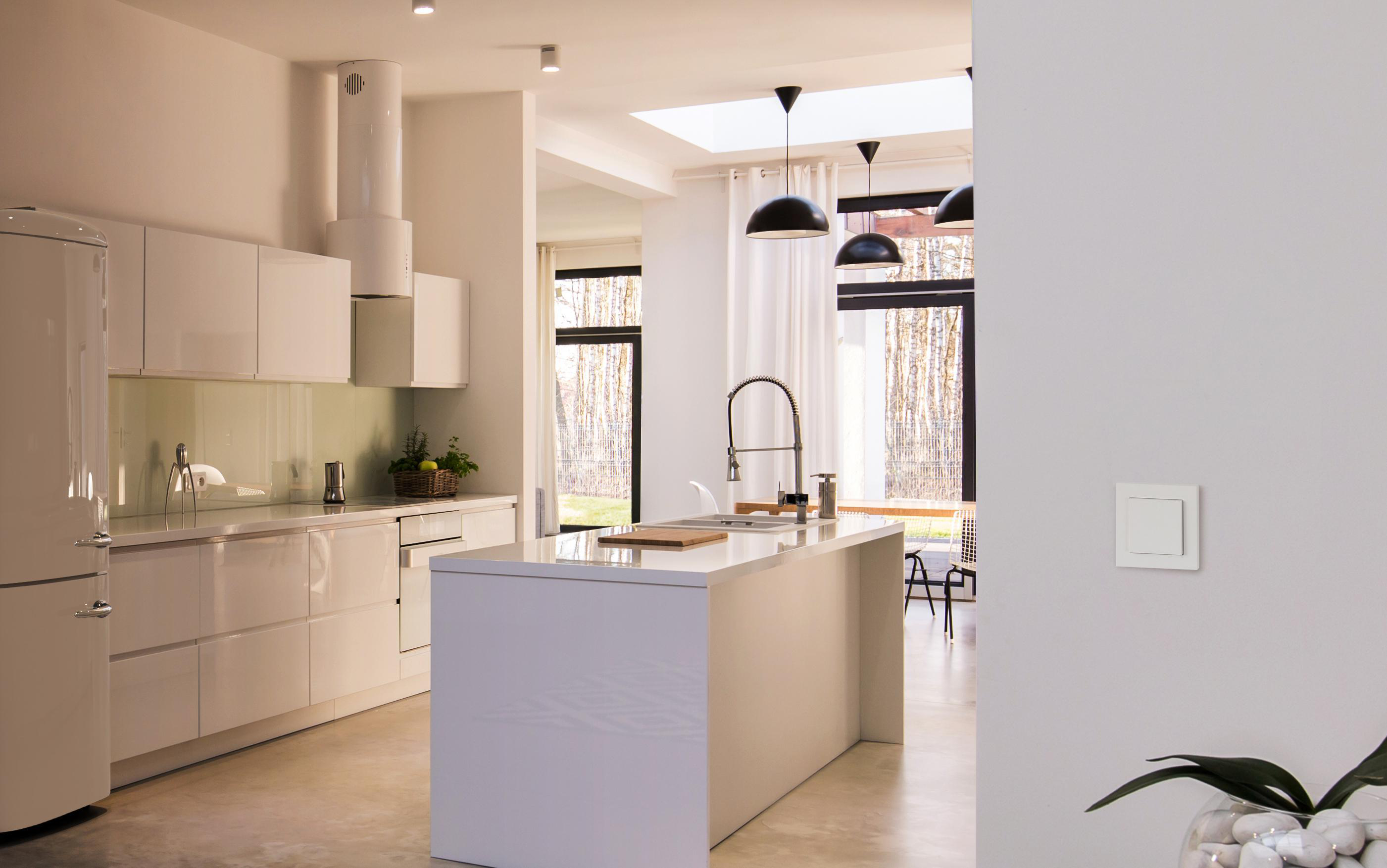 Moderne weiße Küche mit Insel, weißen Schränken und großem Fenster.