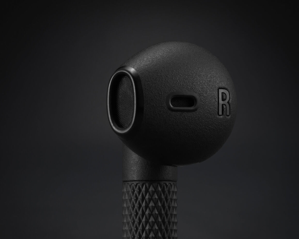 Close-up van een zwarte oortelefoon met de letter 'R' en mesh.