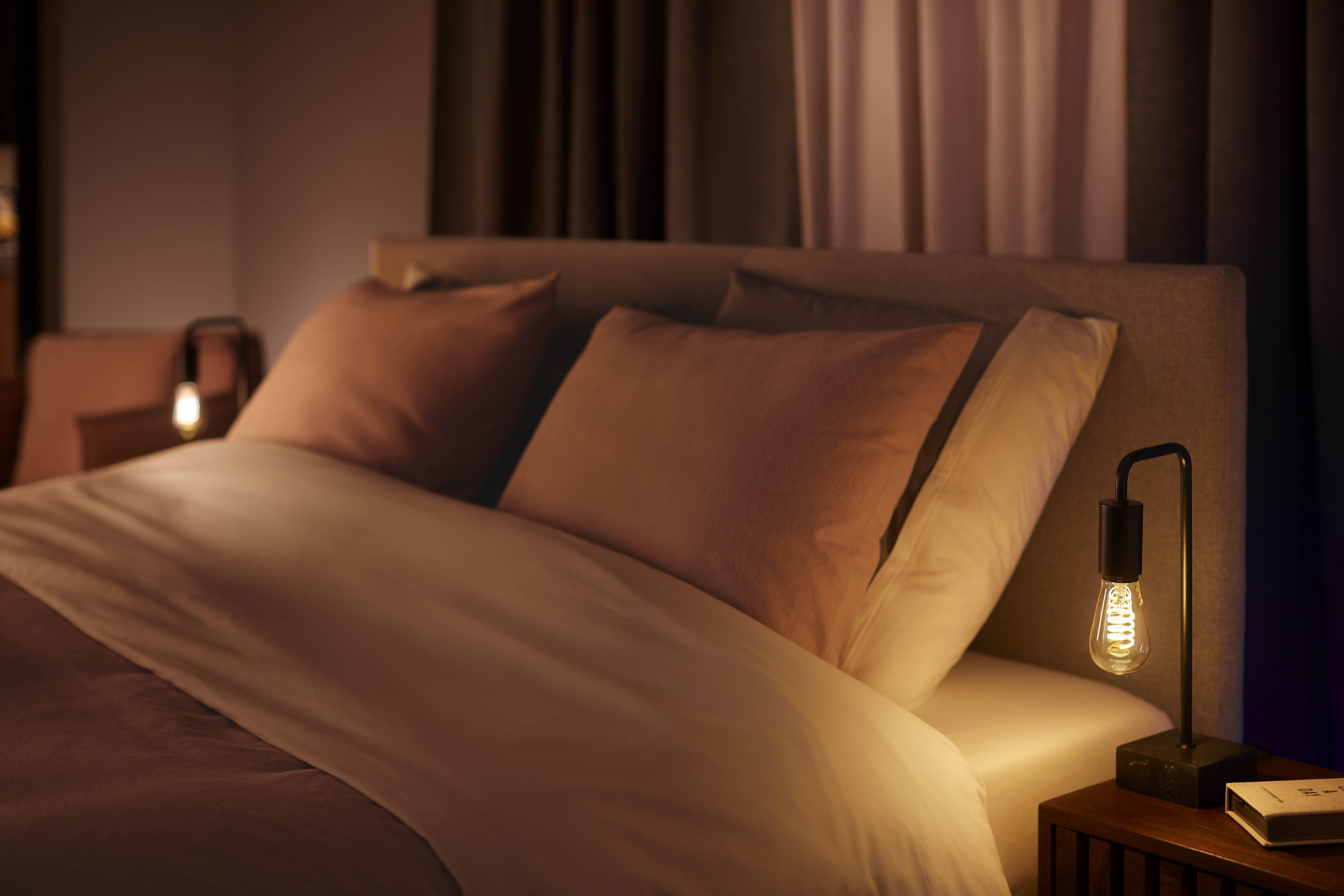 Schlafzimmer mit Bett, Lampen und Kissen mit warmer, beleuchteter Atmosphäre.