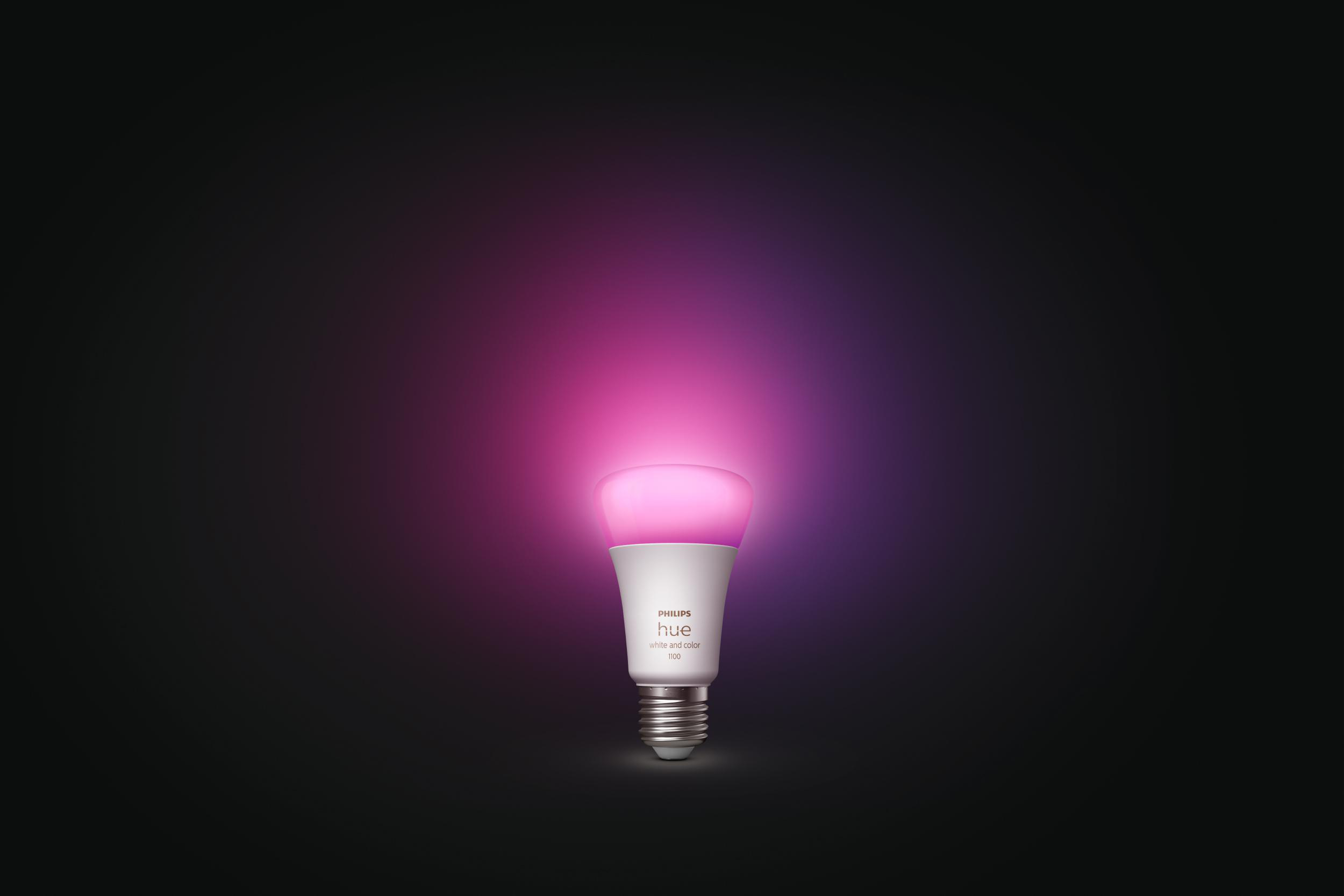 Eine Philips Hue Smart-Glühbirne, die rosa und violettes Licht vor einem schwarzen Hintergrund ausstrahlt.