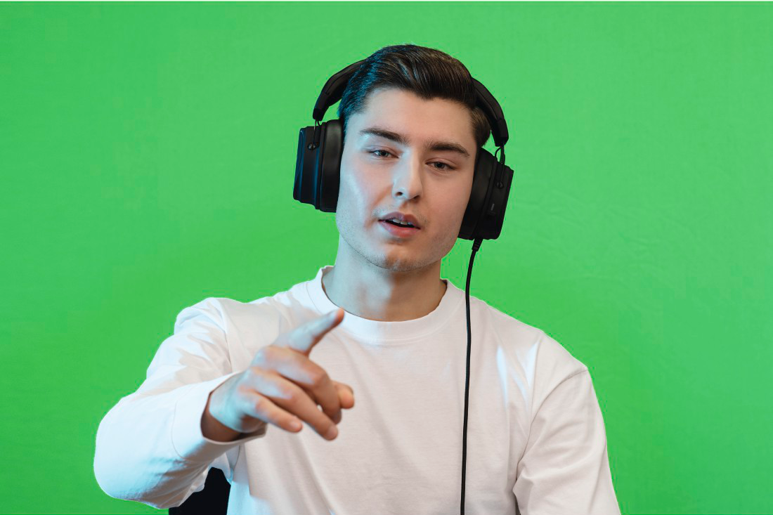 Un jeune homme avec un casque et une chemise blanche montre le spectateur contre un écran vert.