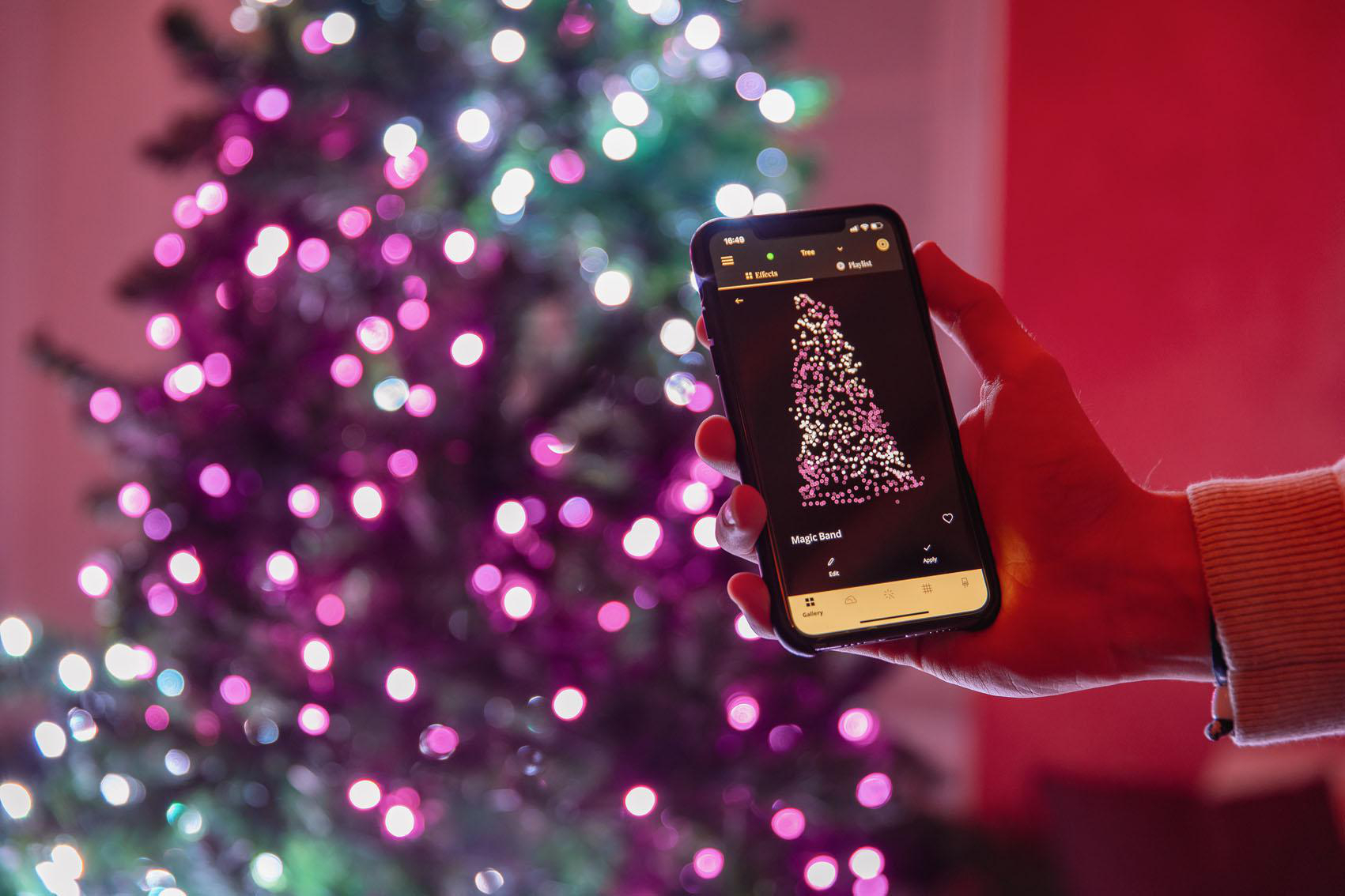 Eine Person hält ein Telefon, das ein Weihnachtsbaumdesign mit bunten Lichtern zeigt.