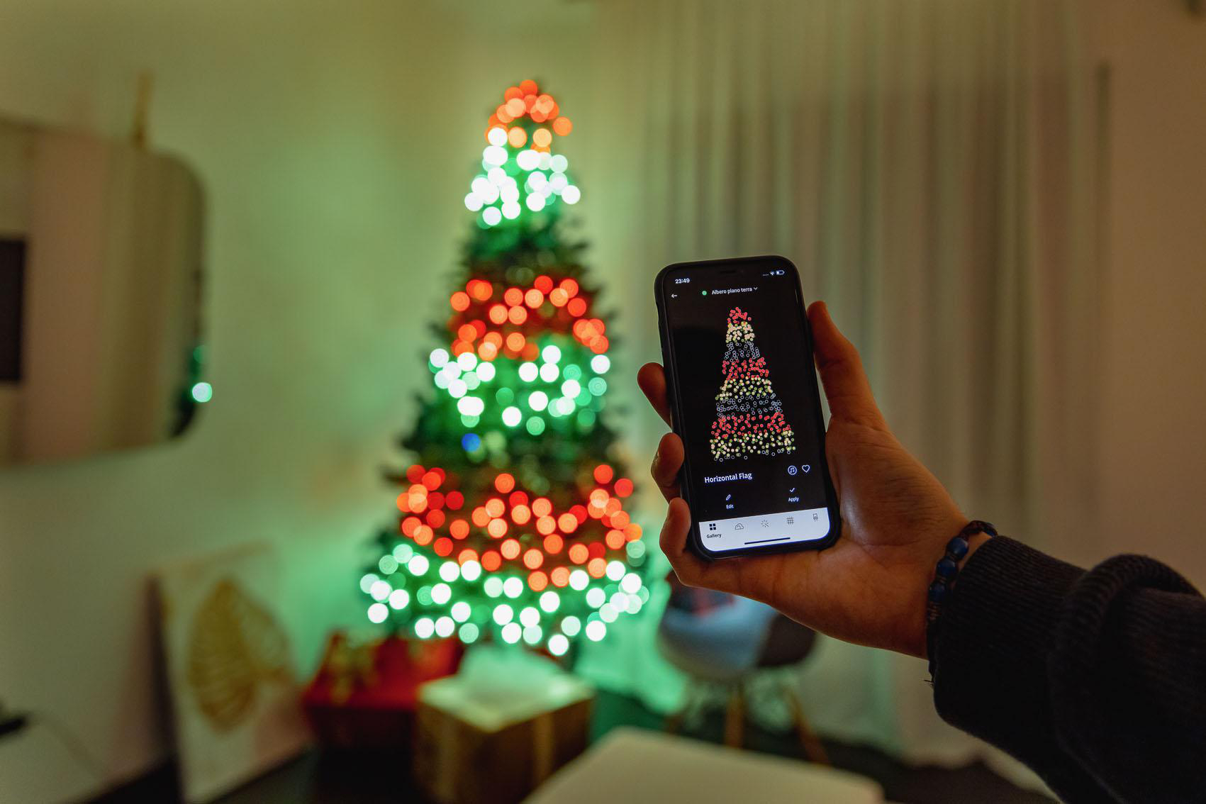 Handy, das einen Weihnachtsbaum mit roten, grünen und weißen Lichtern zeigt. Der Baum steht in einem Raum.