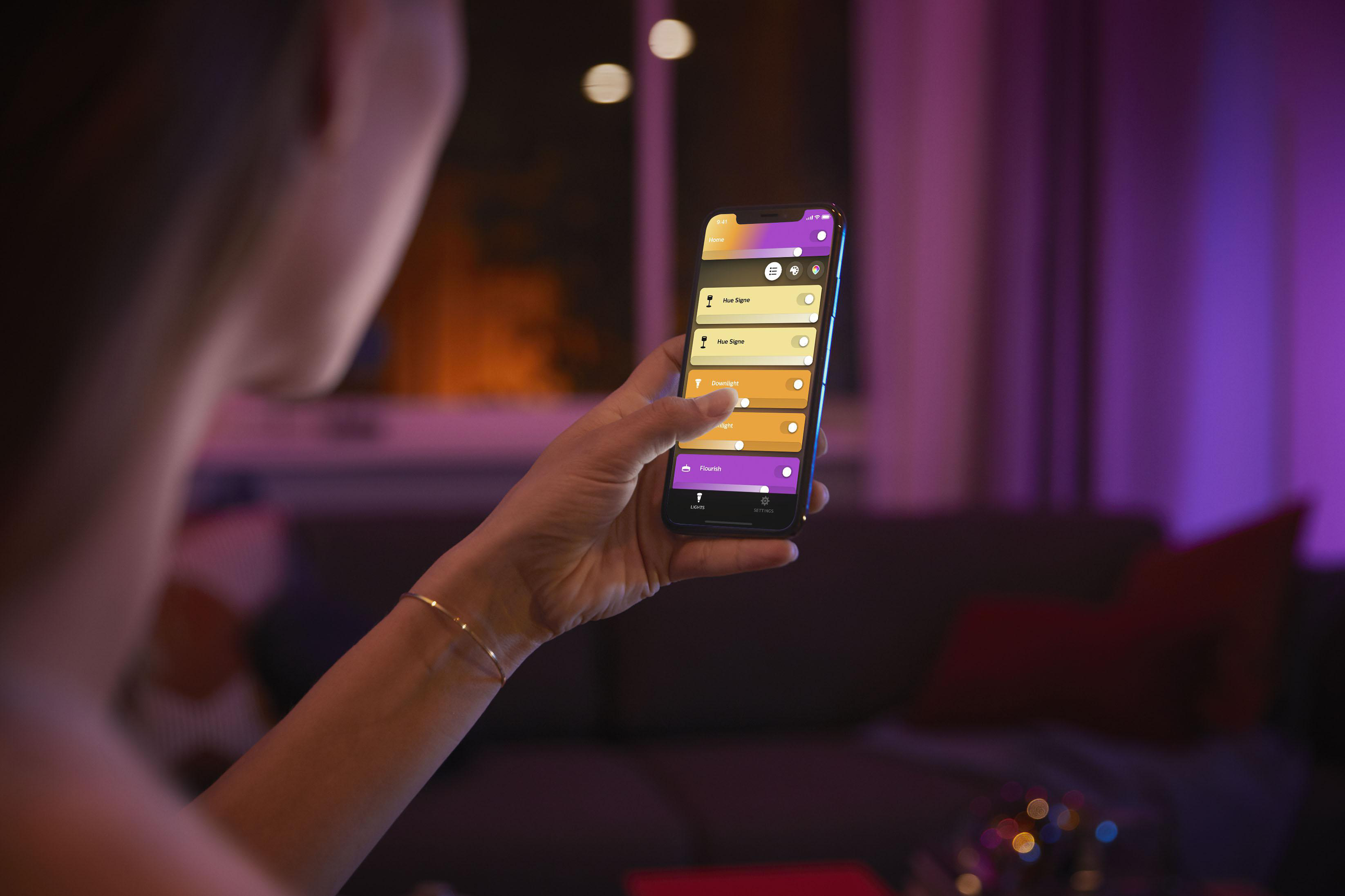 Frau hält ein Smartphone und verwendet eine Smart-Home-App, um die Lichter zu steuern.
