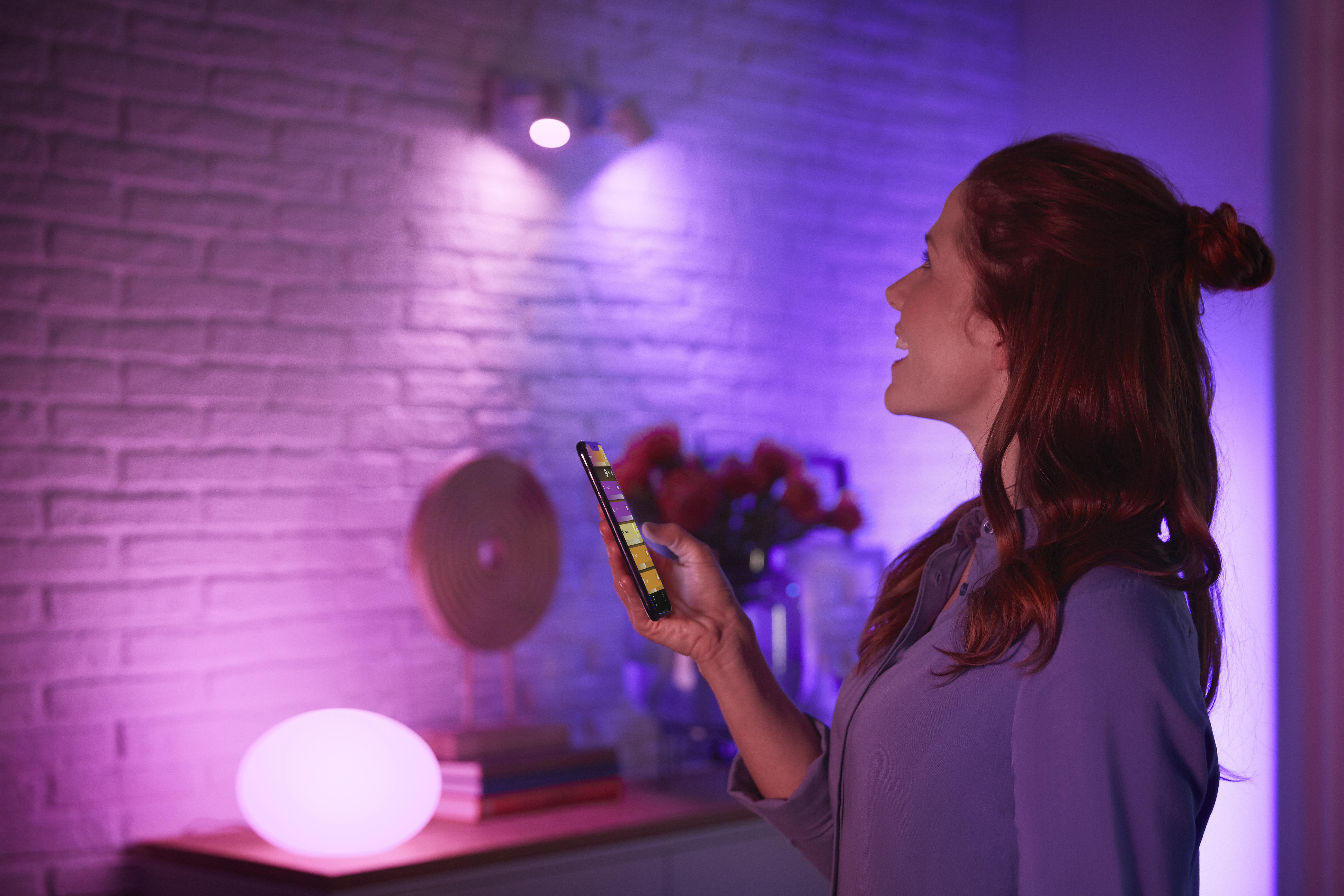 Frau benutzt Smartphone, farbig beleuchteter Raum mit runder Lampe.