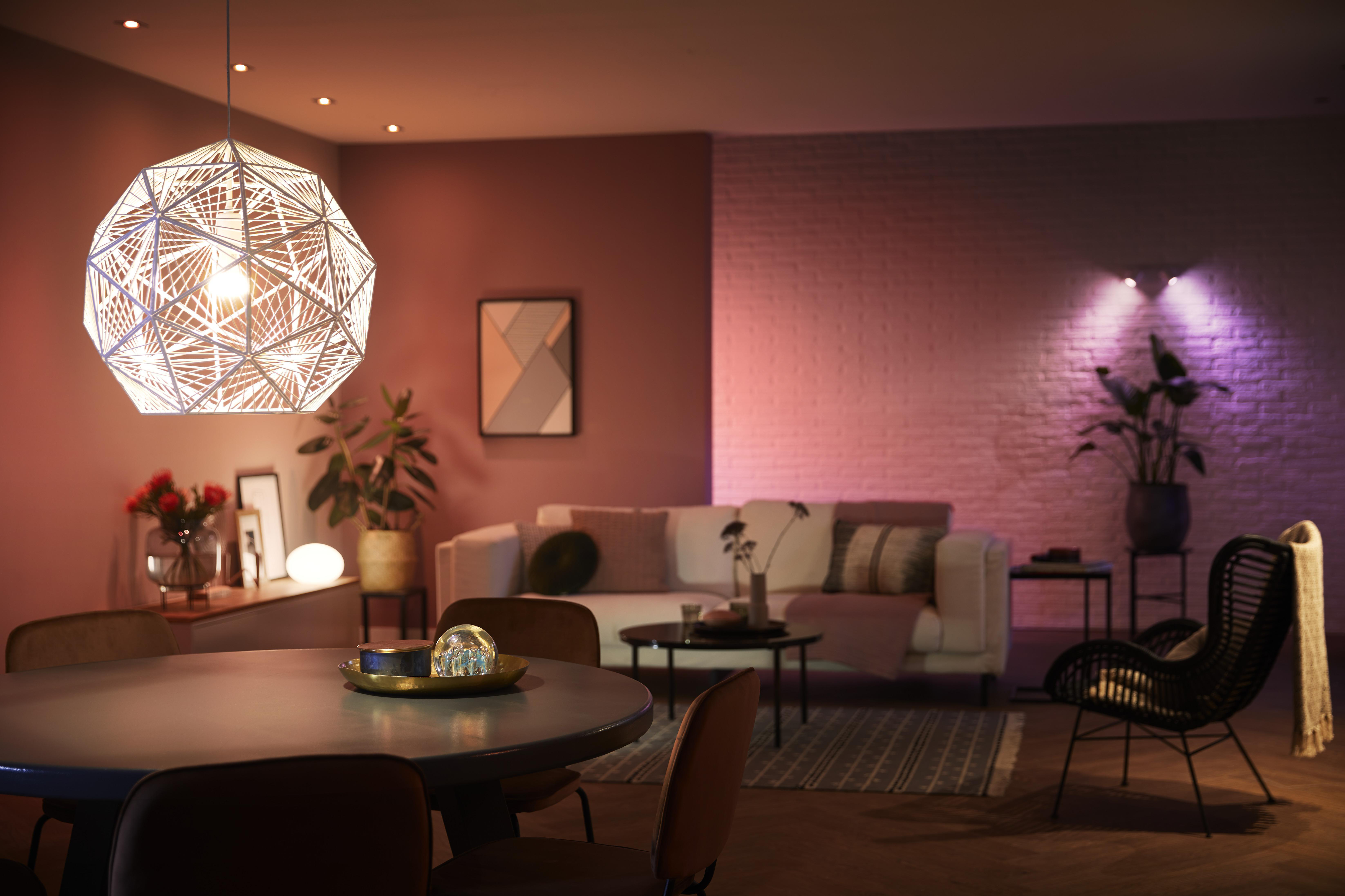 Wohnzimmer mit rundem Tisch, Sofa und Pendelleuchte. Warme Beleuchtung und dunkle Töne.