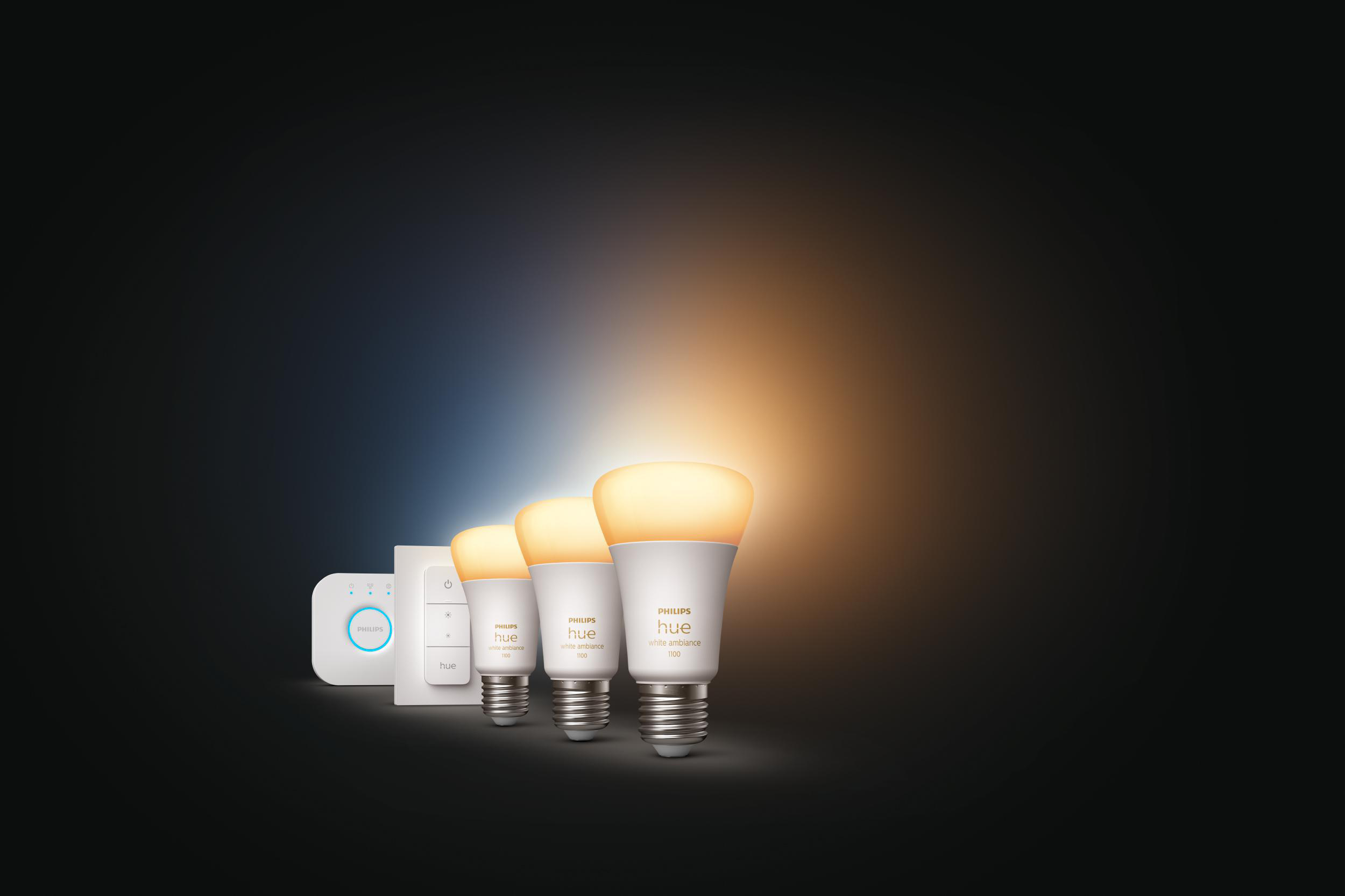 Drei Philips Hue Smart-Glühbirnen und eine Bridge auf dunklem Hintergrund. Glühbirnen sind an.