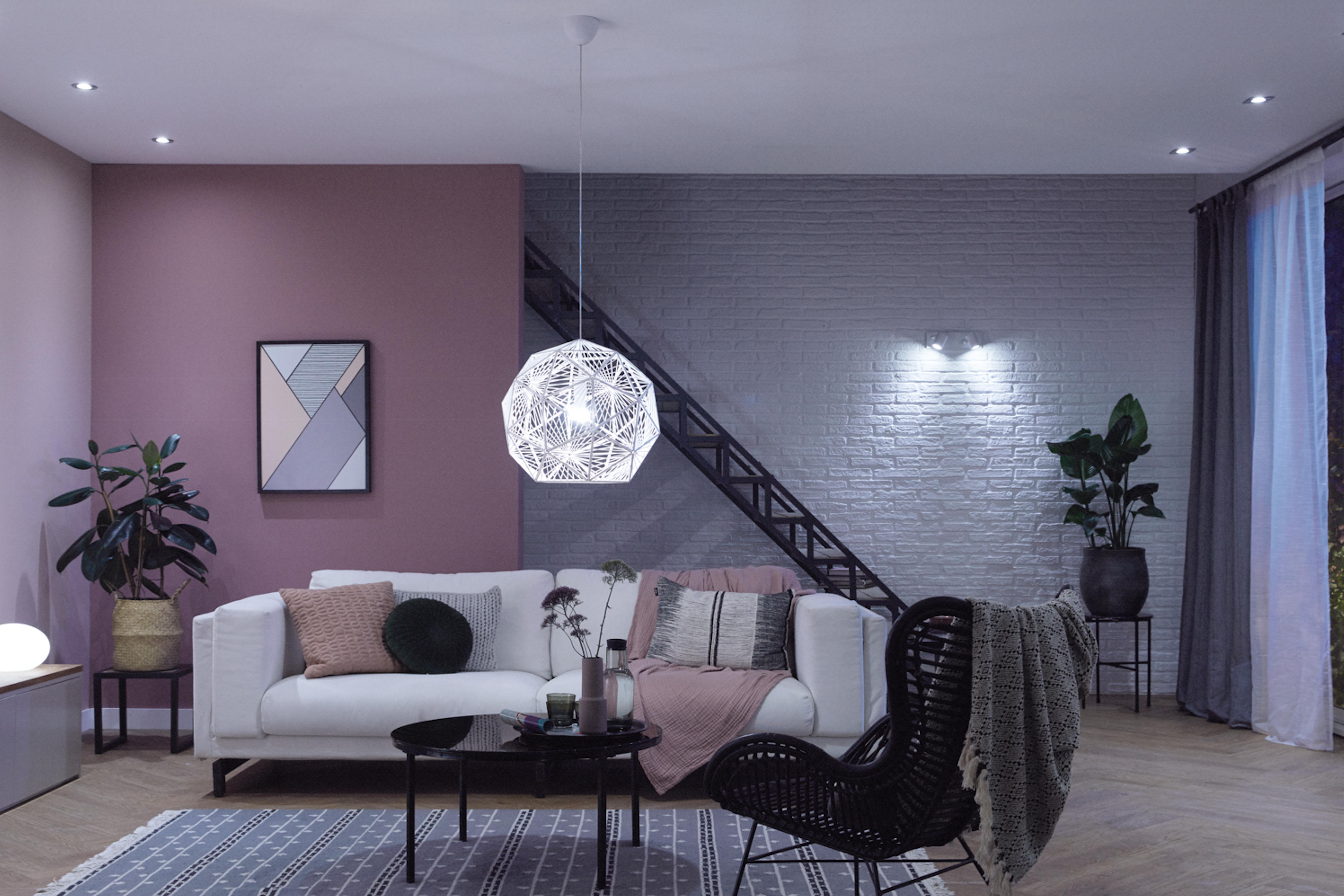 Wohnzimmer mit weißem Sofa, Pflanzen und moderner Beleuchtung. Rosa und graue Wände.
