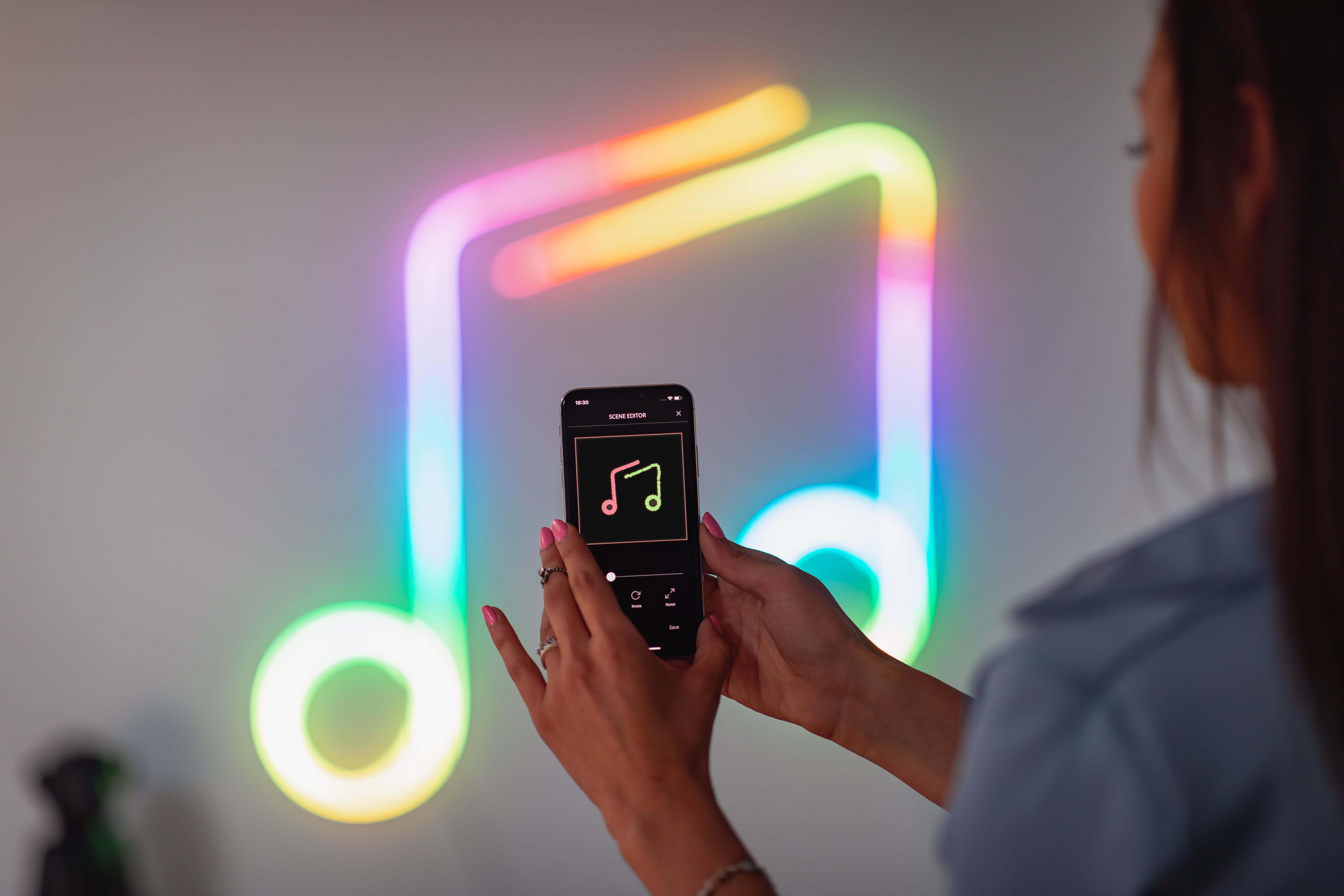 Frau hält Smartphone, zeigt Musiknoten-Grafik an der Wand.