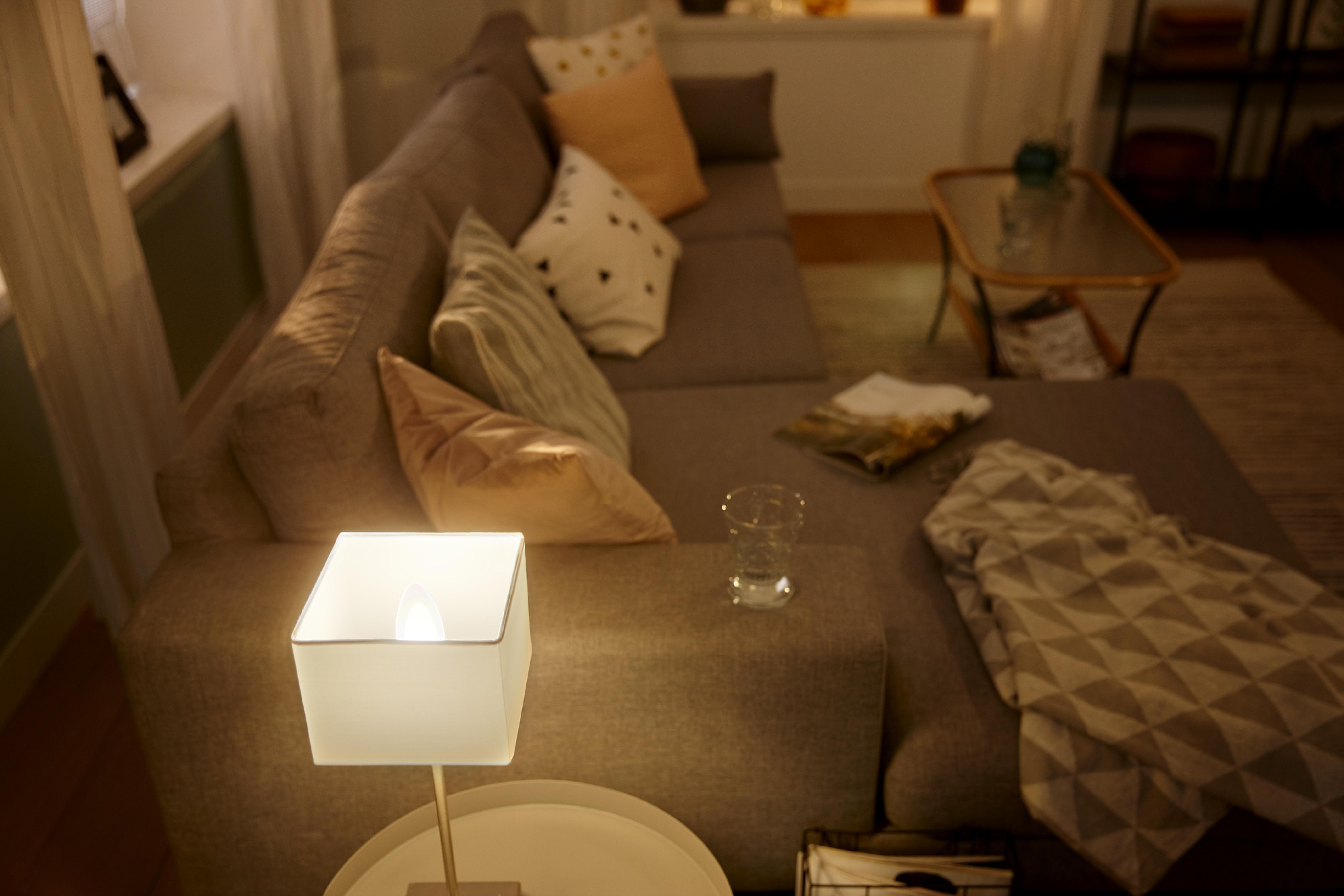 Wohnzimmer mit grauem Sofa, Lampe, Couchtisch und einem Glas Wasser.