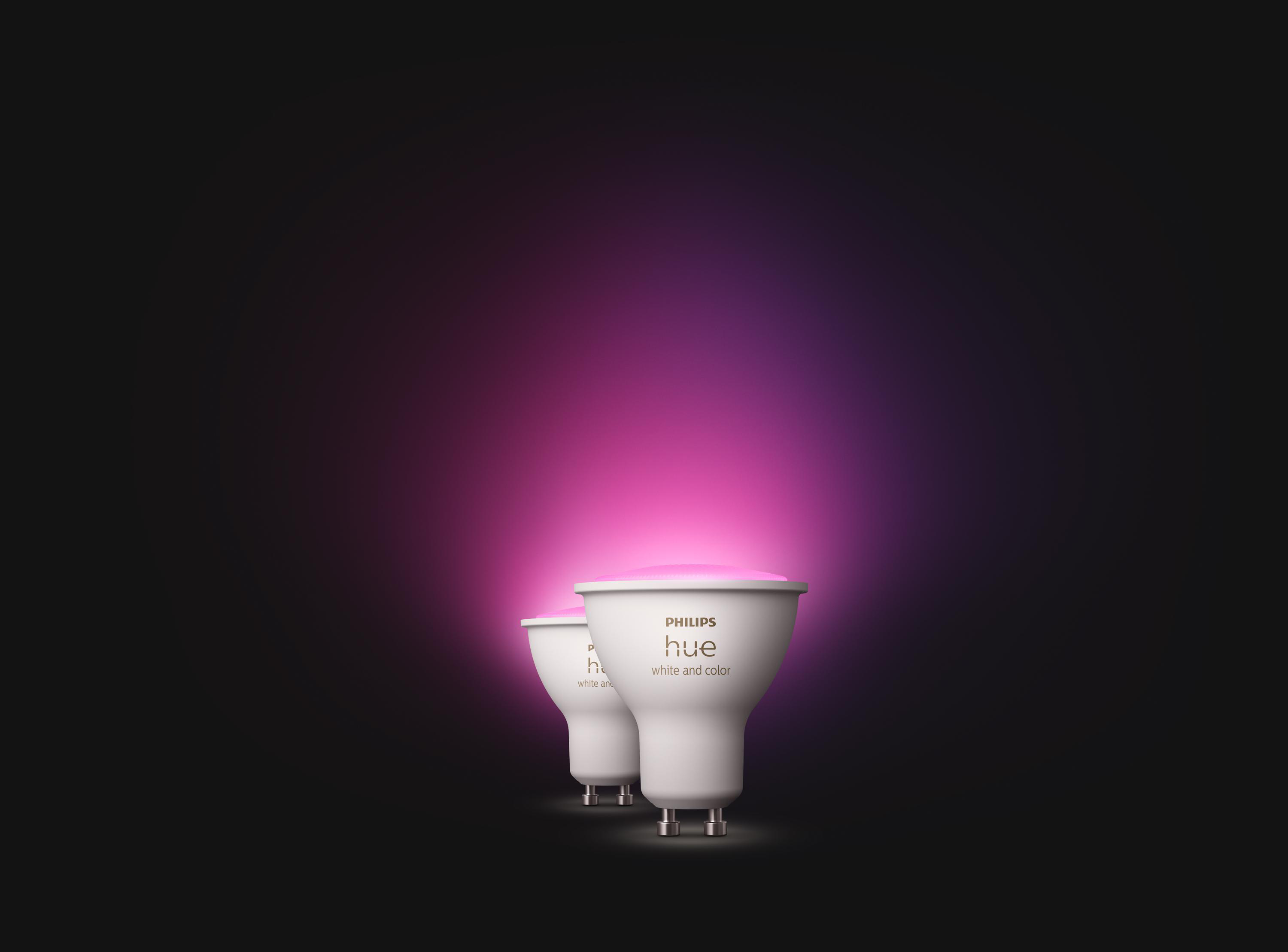 Zwei weiße Philips Hue Smart-Glühbirnen mit rosa und lila Licht vor schwarzem Hintergrund.