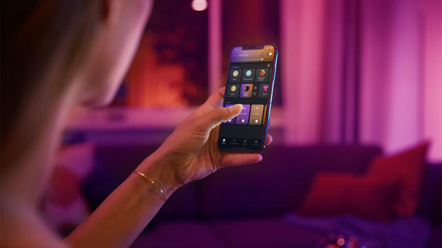 Eine Person, die ein Telefon mit einer Smart-Home-App-Oberfläche hält.