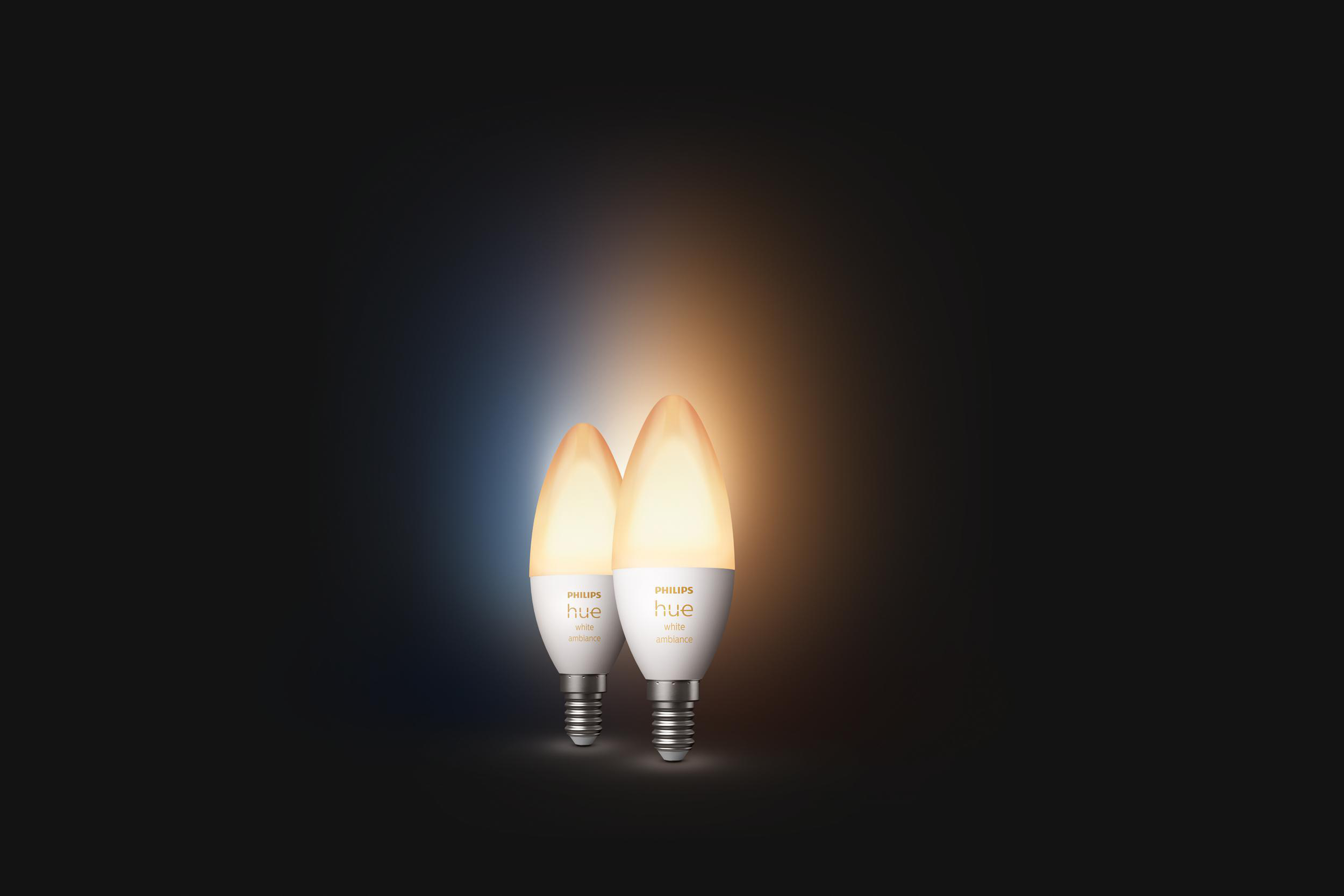Zwei kerzenförmige Smart-Glühbirnen, die gelbes Licht auf dunklem Hintergrund aussenden, Marke Philips Hue sichtbar.