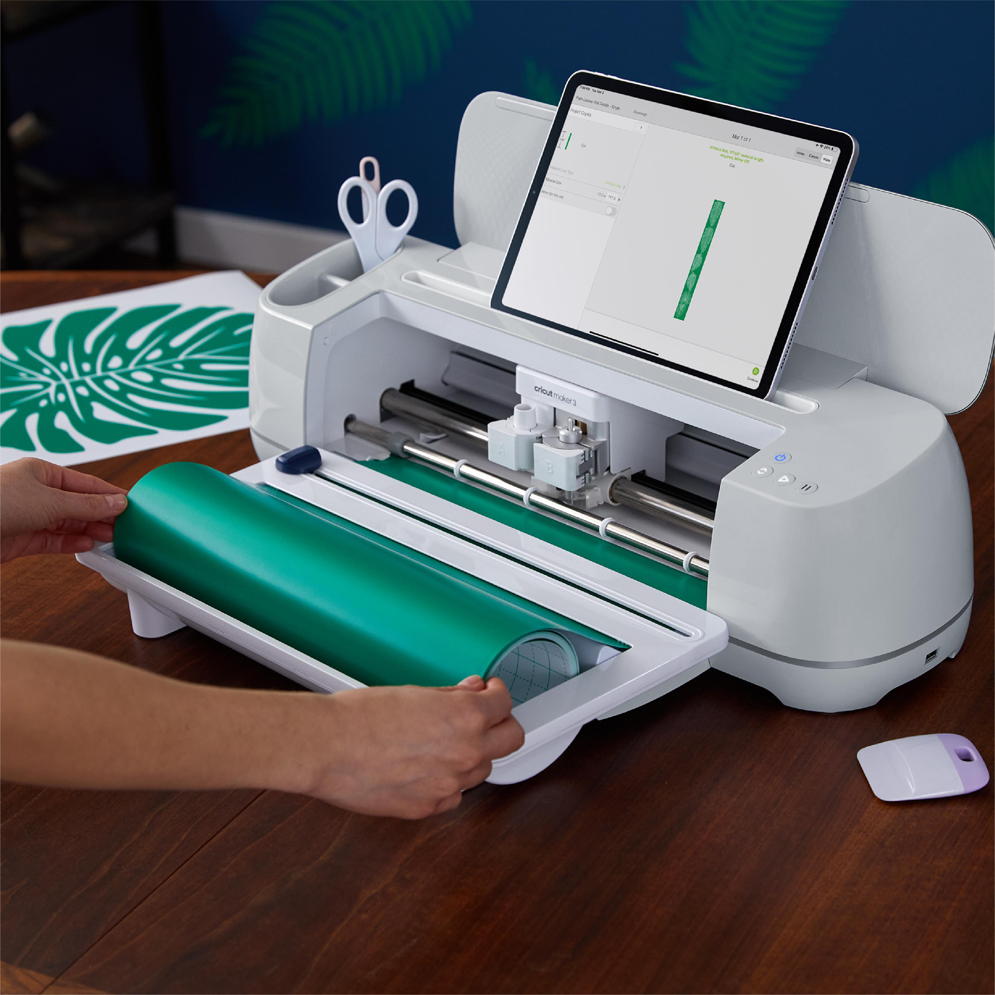 Eine Cricut-Maschine mit Tablet. Grünes Vinyl wird geladen. Schere und Schaber sind vorhanden.