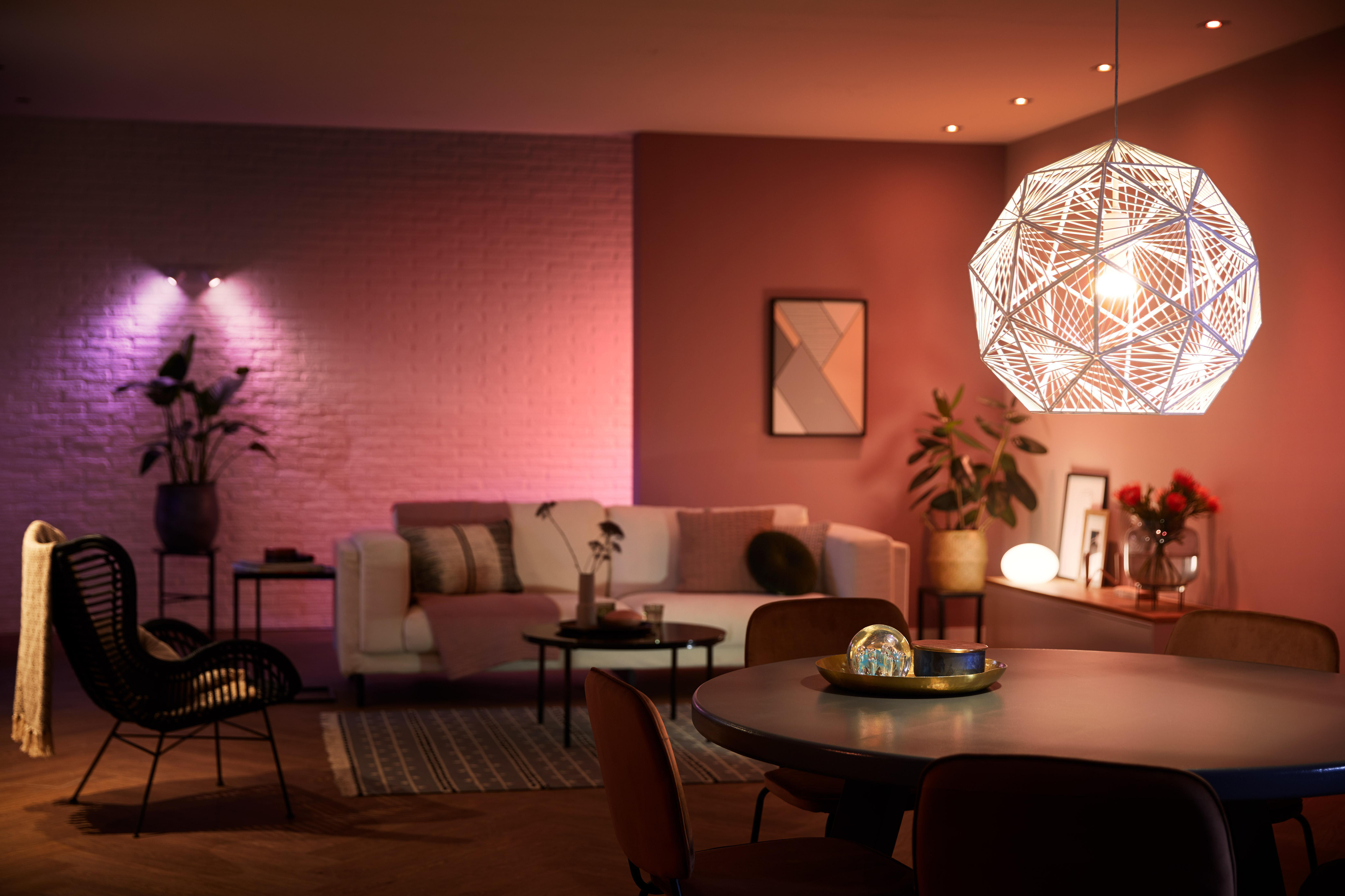 Wohnzimmer mit rosa und weißen Lichtern beleuchtet. Ein weißes Sofa und Pflanzen sind im Raum.