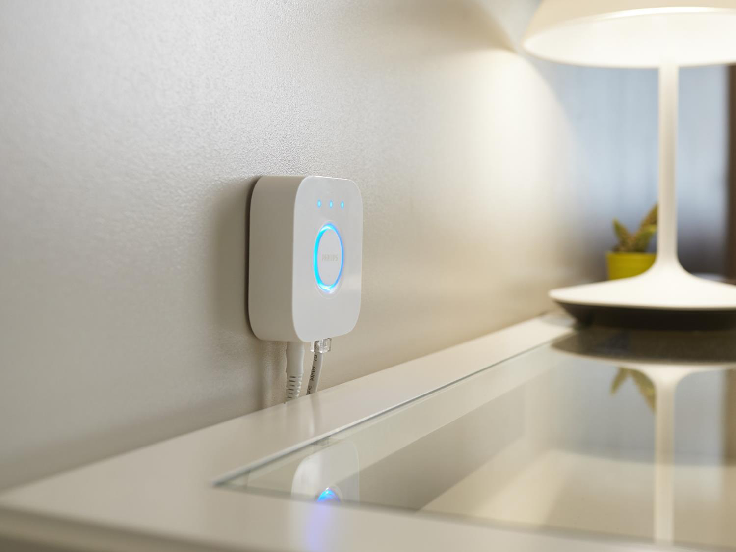 Weißer, quadratischer Smart-Hub an einer Wand mit zwei angeschlossenen Kabeln.