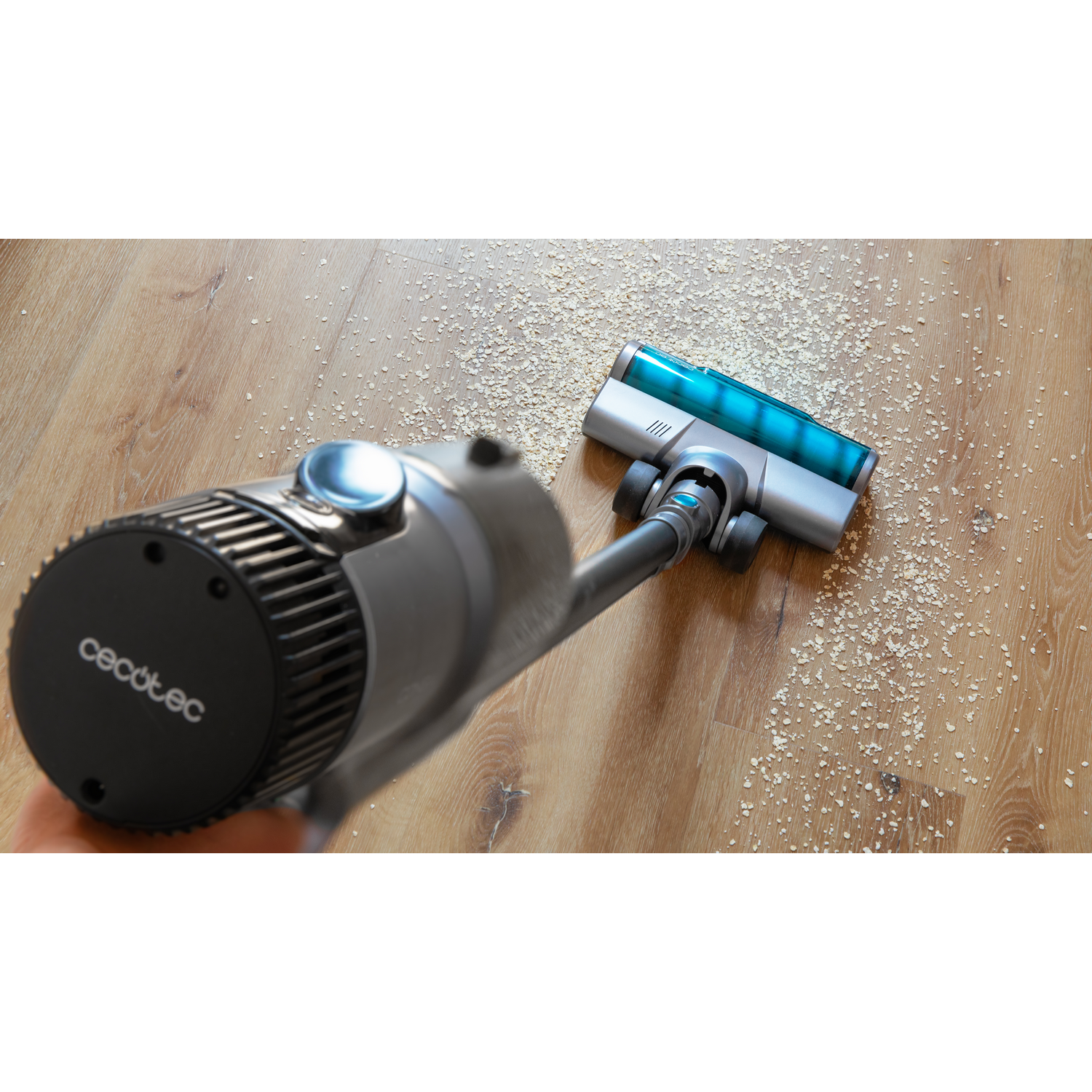 Un cabezal de aspiradora limpiando migas en un piso de madera. El dispositivo es gris y azul.