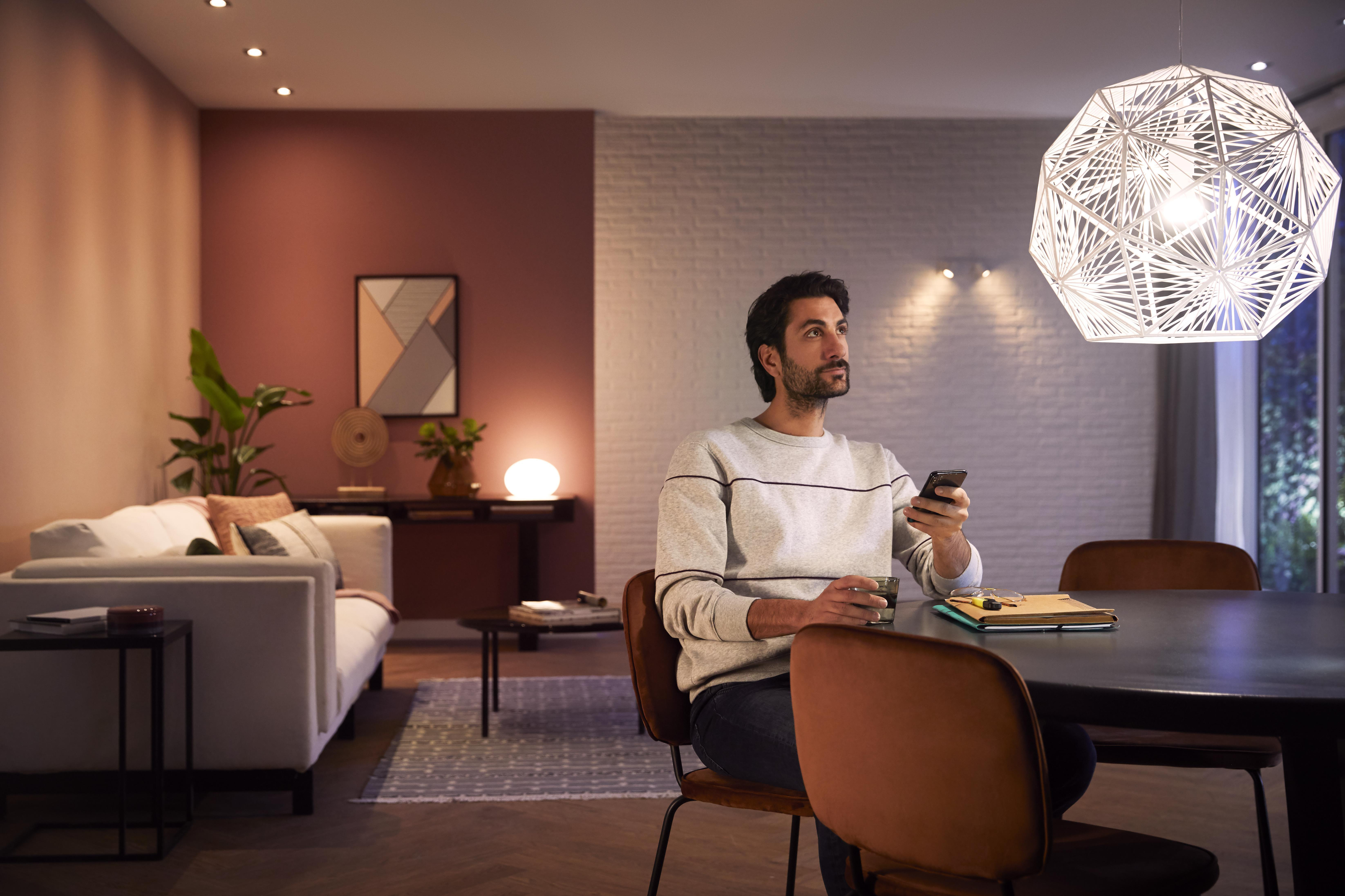 Mann im Wohnzimmer, der auf sein Telefon schaut. Zimmer mit Sofa, Tisch und dekorativer Leuchte.