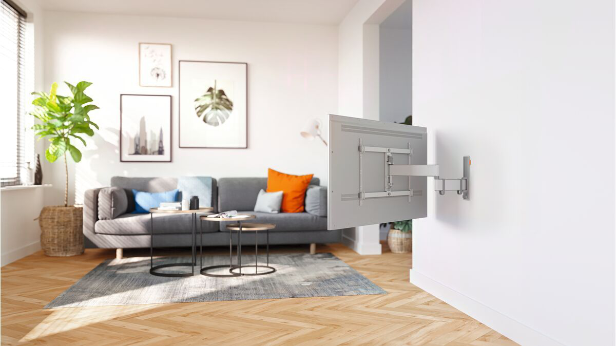 TV montata a parete, con un ambiente soggiorno. Divano e decorazioni sullo sfondo.