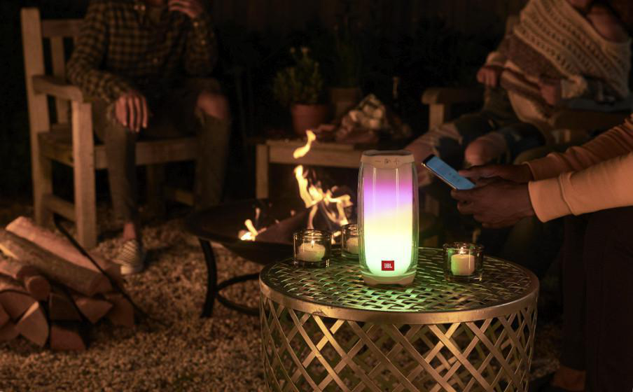Beleuchteter JBL-Lautsprecher mit Personen und Feuer im Hintergrund.