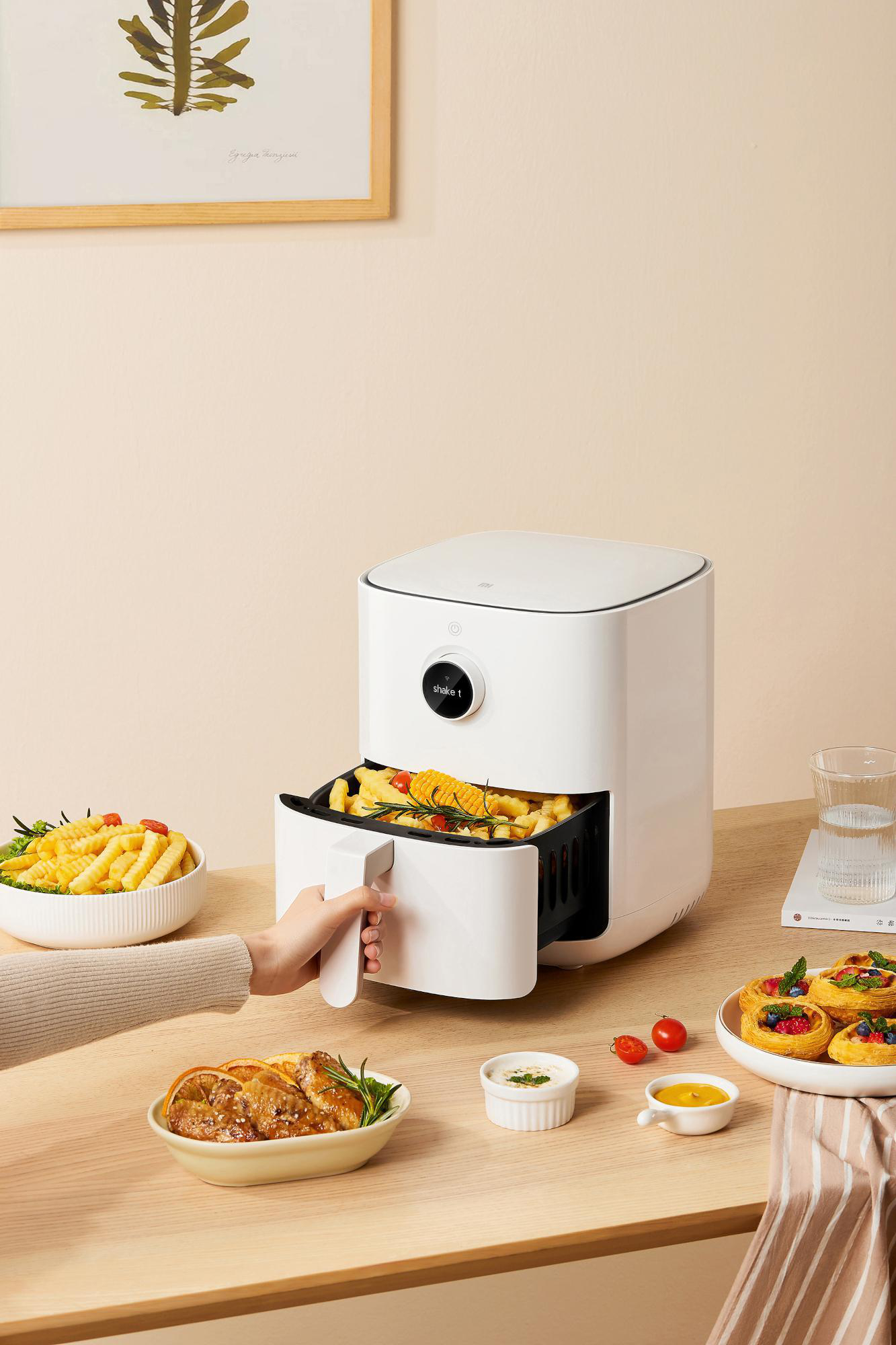 Weißer Airfryer mit Essen. Person hält Schublade, weitere Speisen auf dem Tisch.