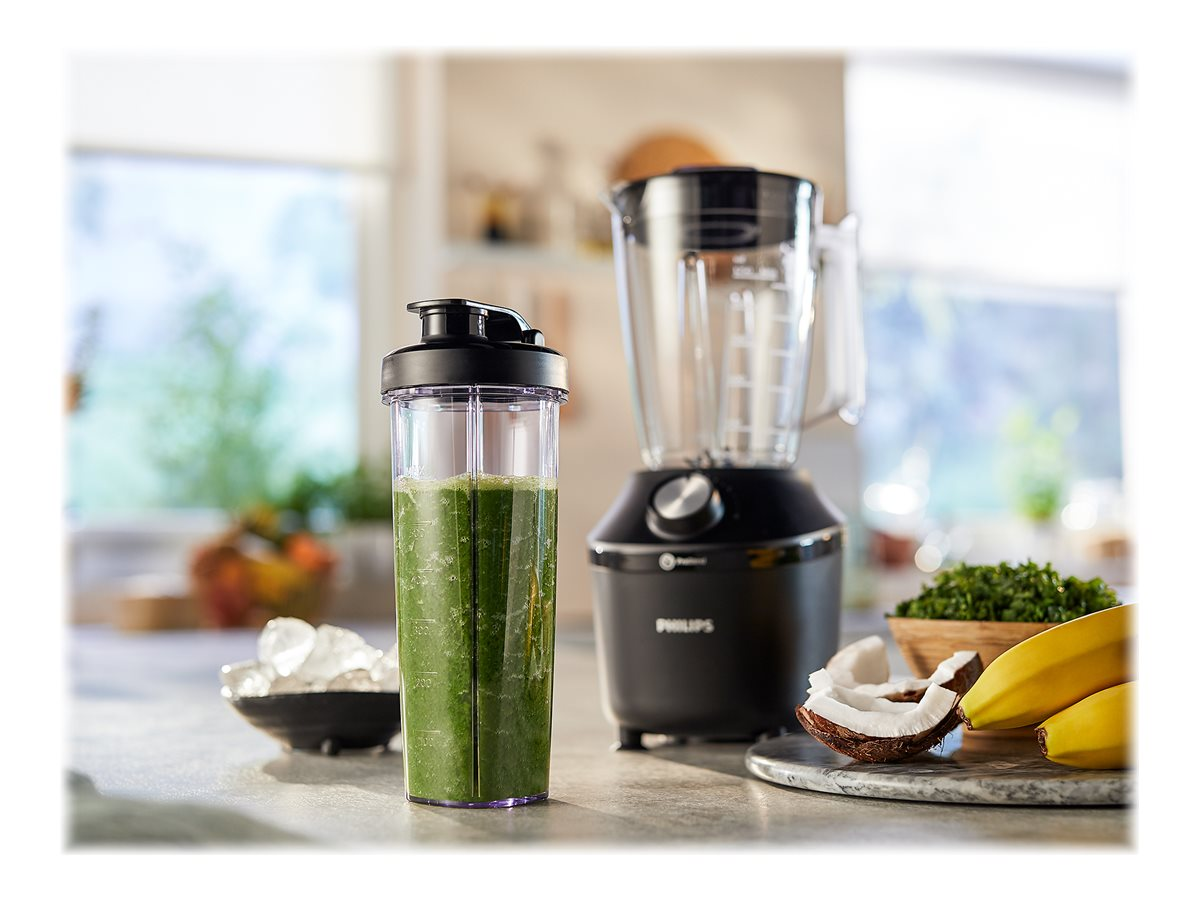 Ein Mixer mit einem grünen Smoothie und Zutaten wie Eis, Kokosnuss und Bananen auf der Theke.