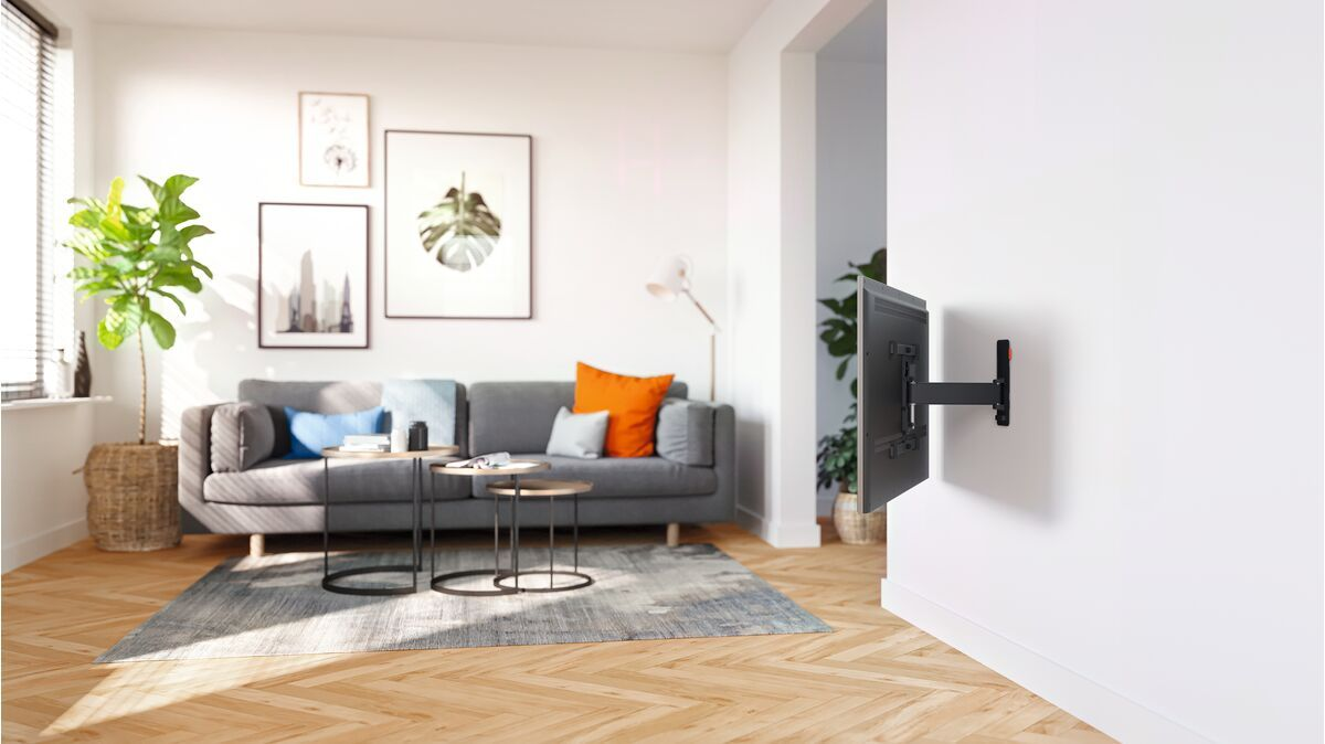 Wohnzimmer mit grauem Sofa, Kunst und einem an der weißen Wand montierten Fernseher. Holzböden.