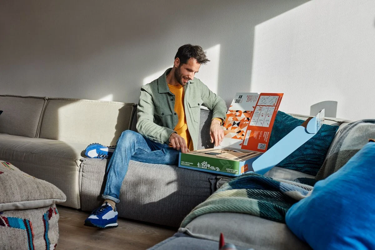 Mann öffnet eine Box auf einem Sofa im Wohnzimmer.