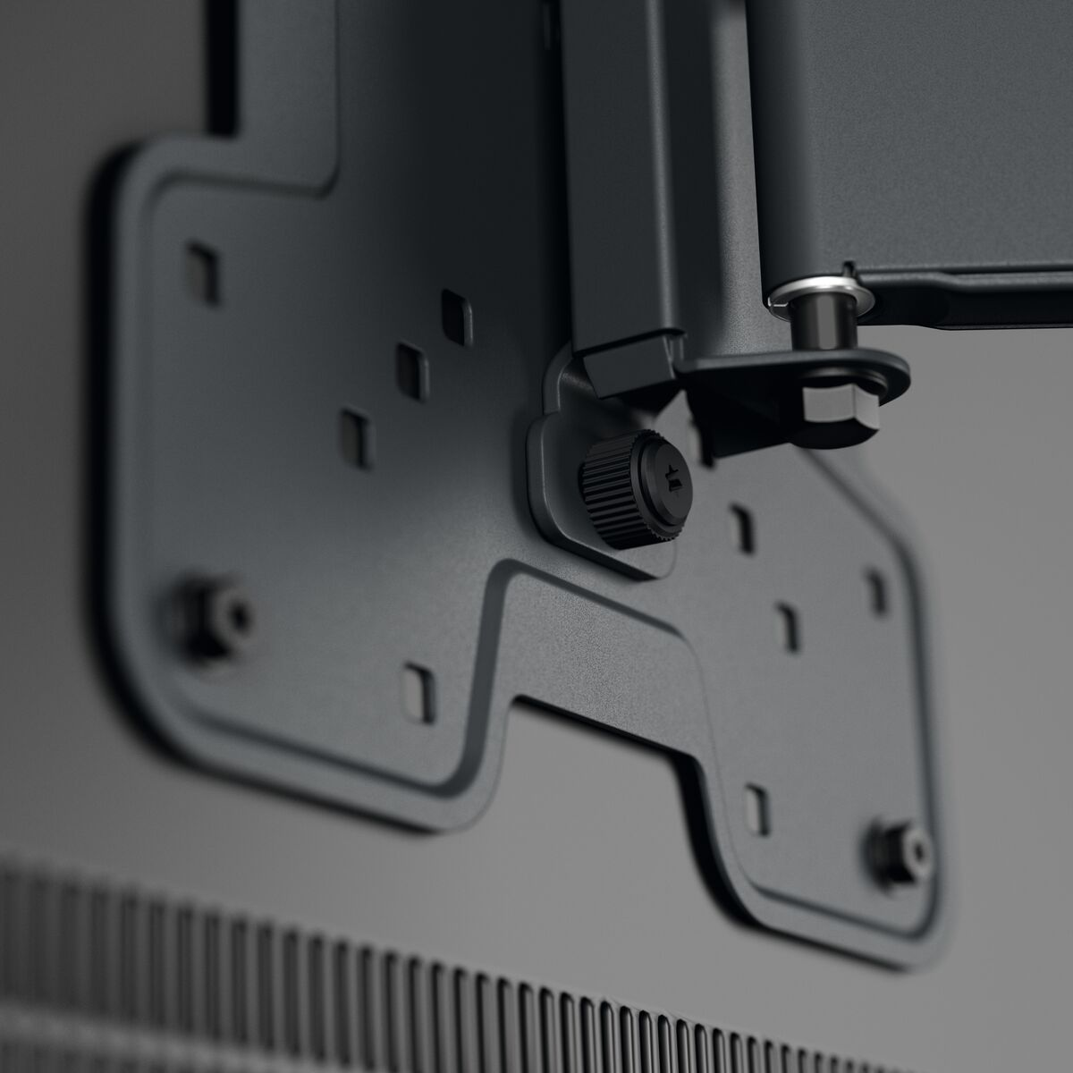 Gros plan sur un support de montage TV noir, avec vis et points de fixation visibles.