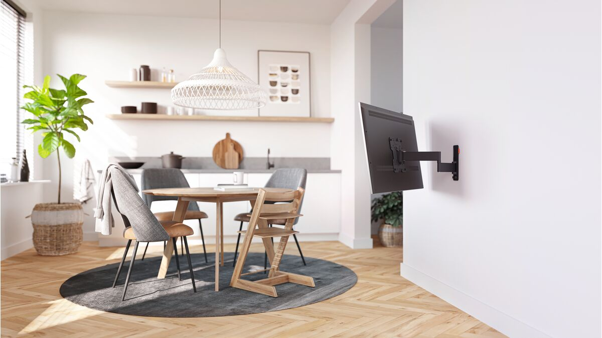 Une cuisine avec une table à manger, des chaises et une télévision murale. Une plante verte dans le coin.